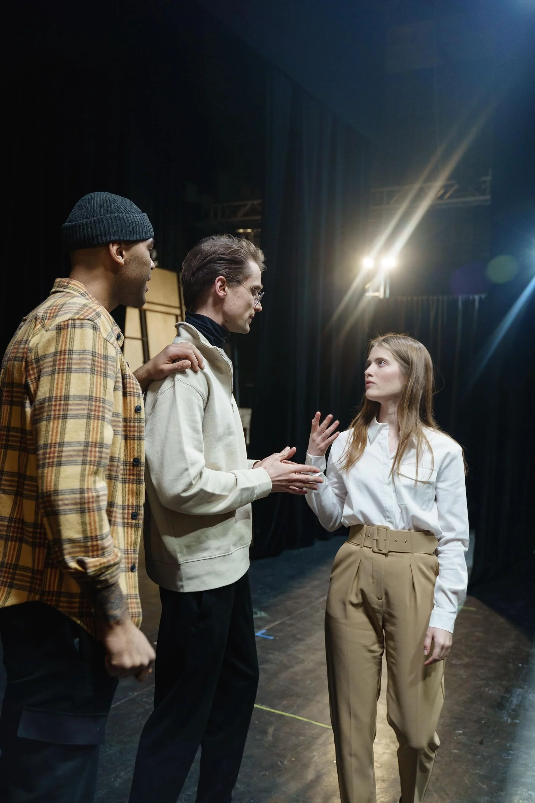 Three actors running a scene together on a dark stage under a single stage light.