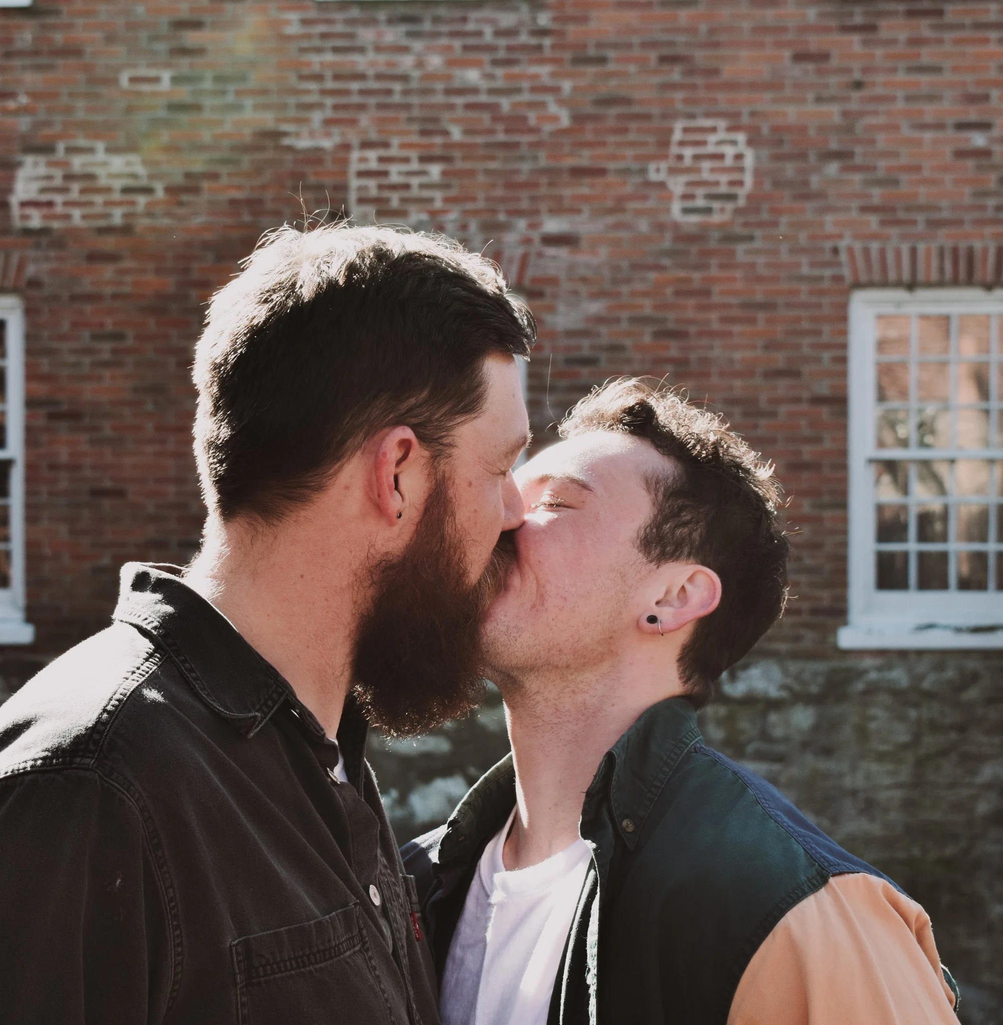 Close-up of three people sharing a kiss outdoors against a brick wall.