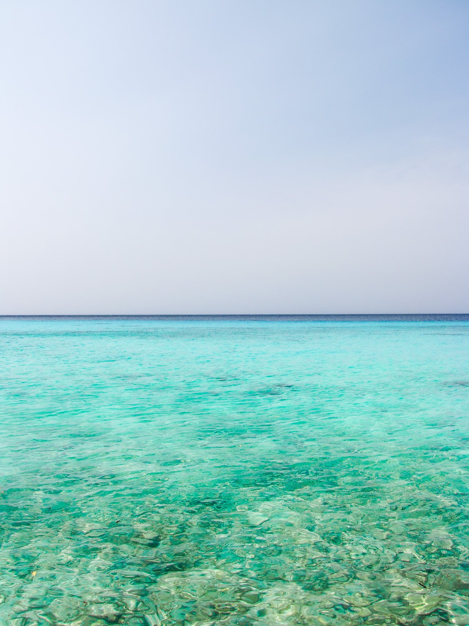 A clear, turquoise sea with gentle waves, under a pale blue sky with some light clouds.
