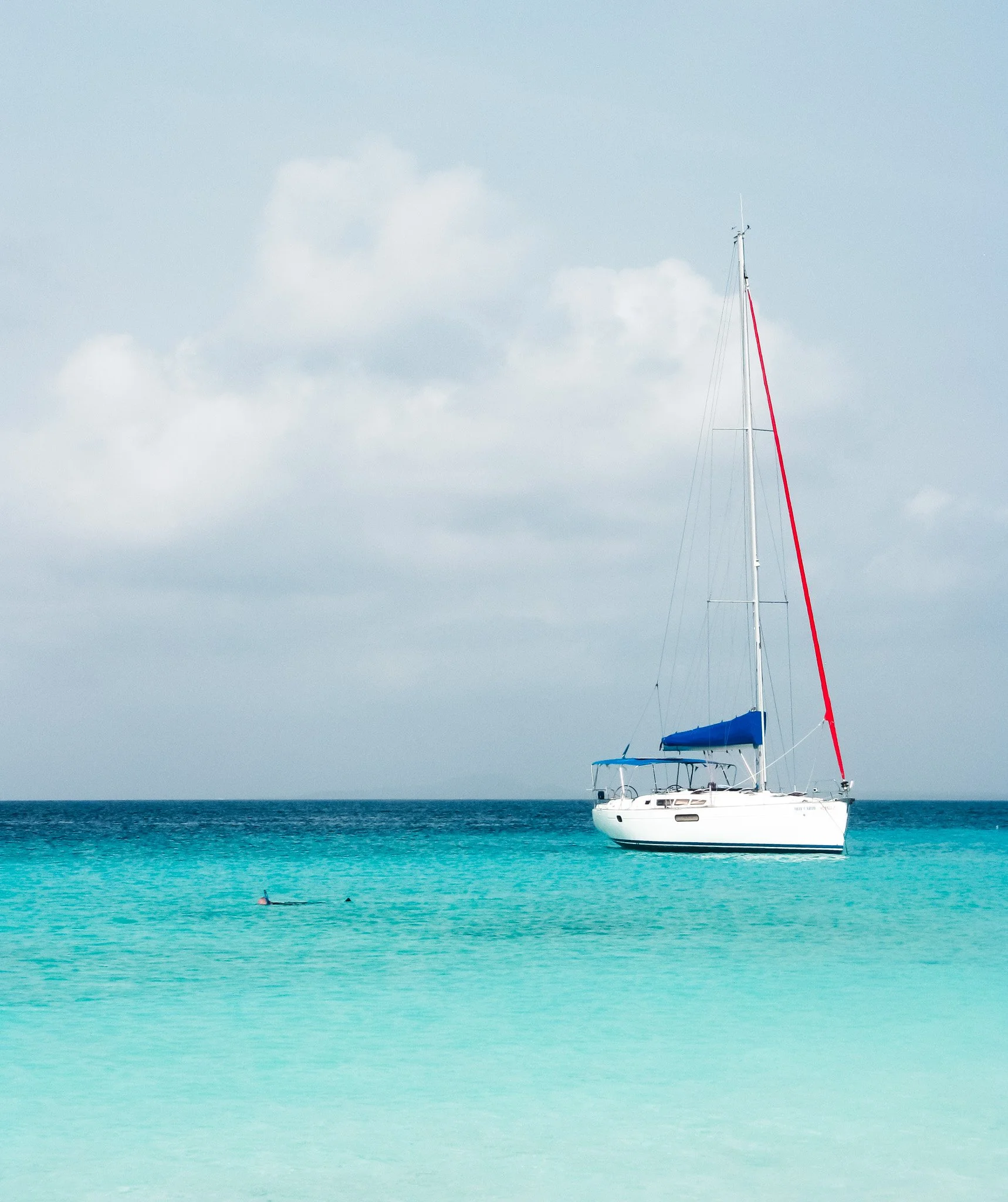 A sailboat floating on turquoise water, with a cloudy sky above.