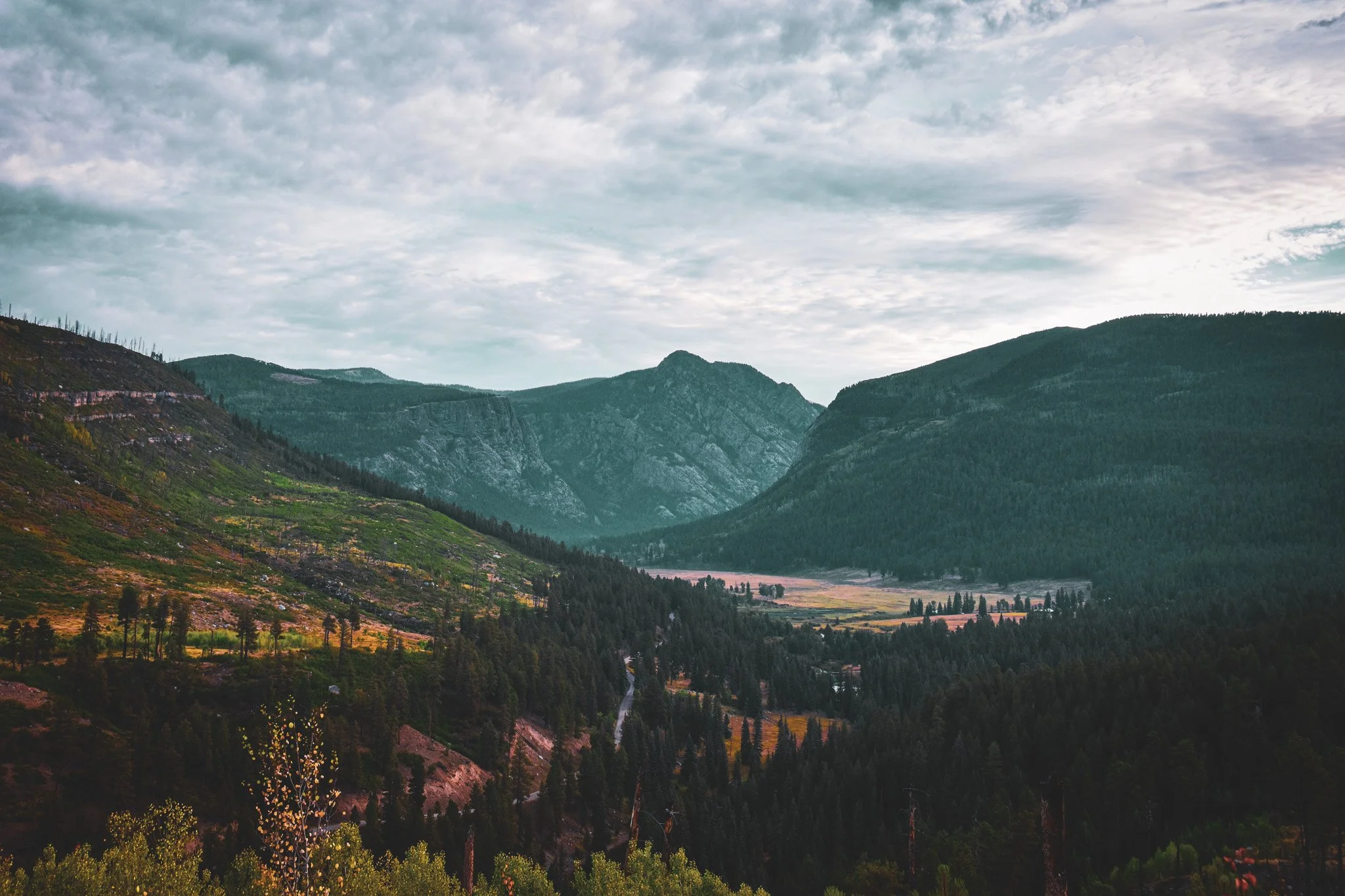 Scenic view of a mountainous landscape with green trees, rolling hills, and a cloudy sky.