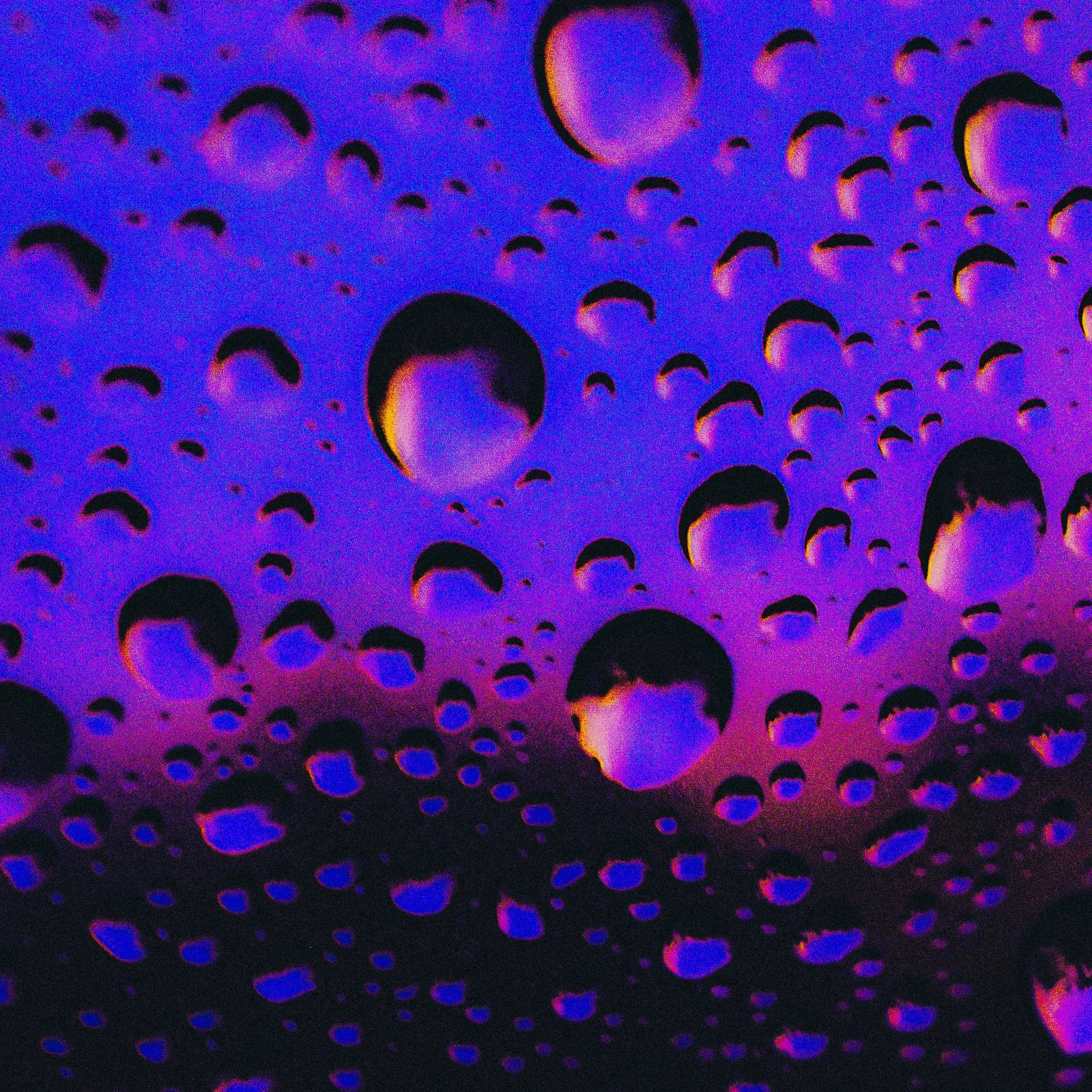 Multiple raindrops on a surface with a dark background and vibrant colors reflecting inside the raindrops.