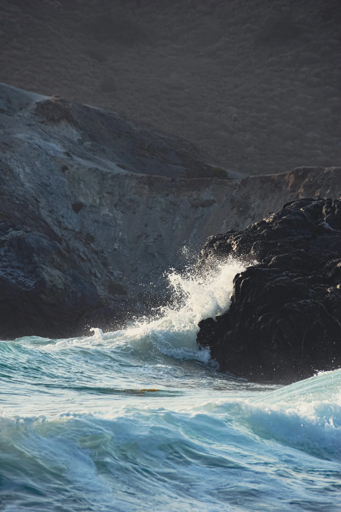Ocean waves crashing against dark rocky cliffs during daytime.