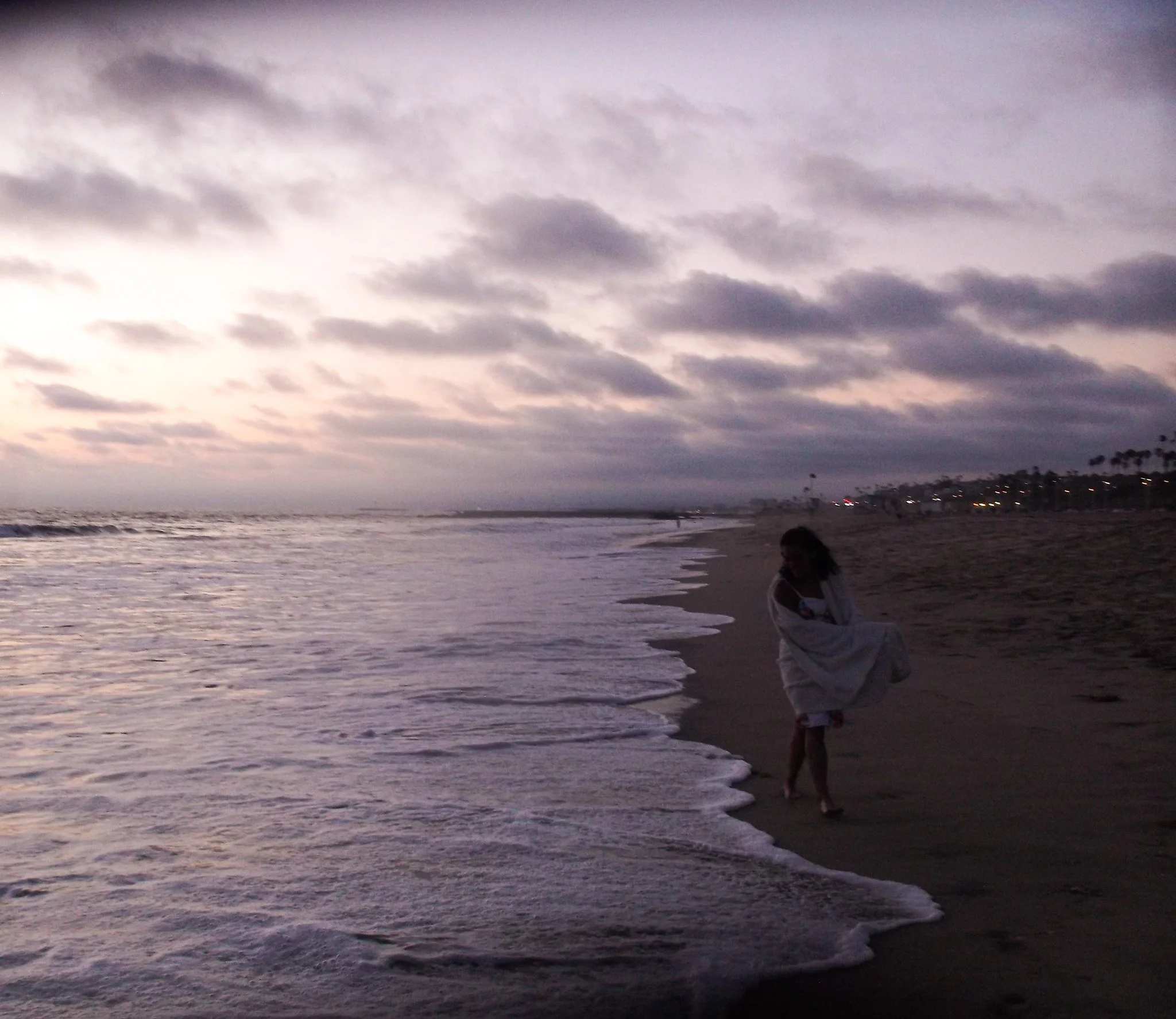 People walking on a beach during dusk with cloudy sky and ocean waves.