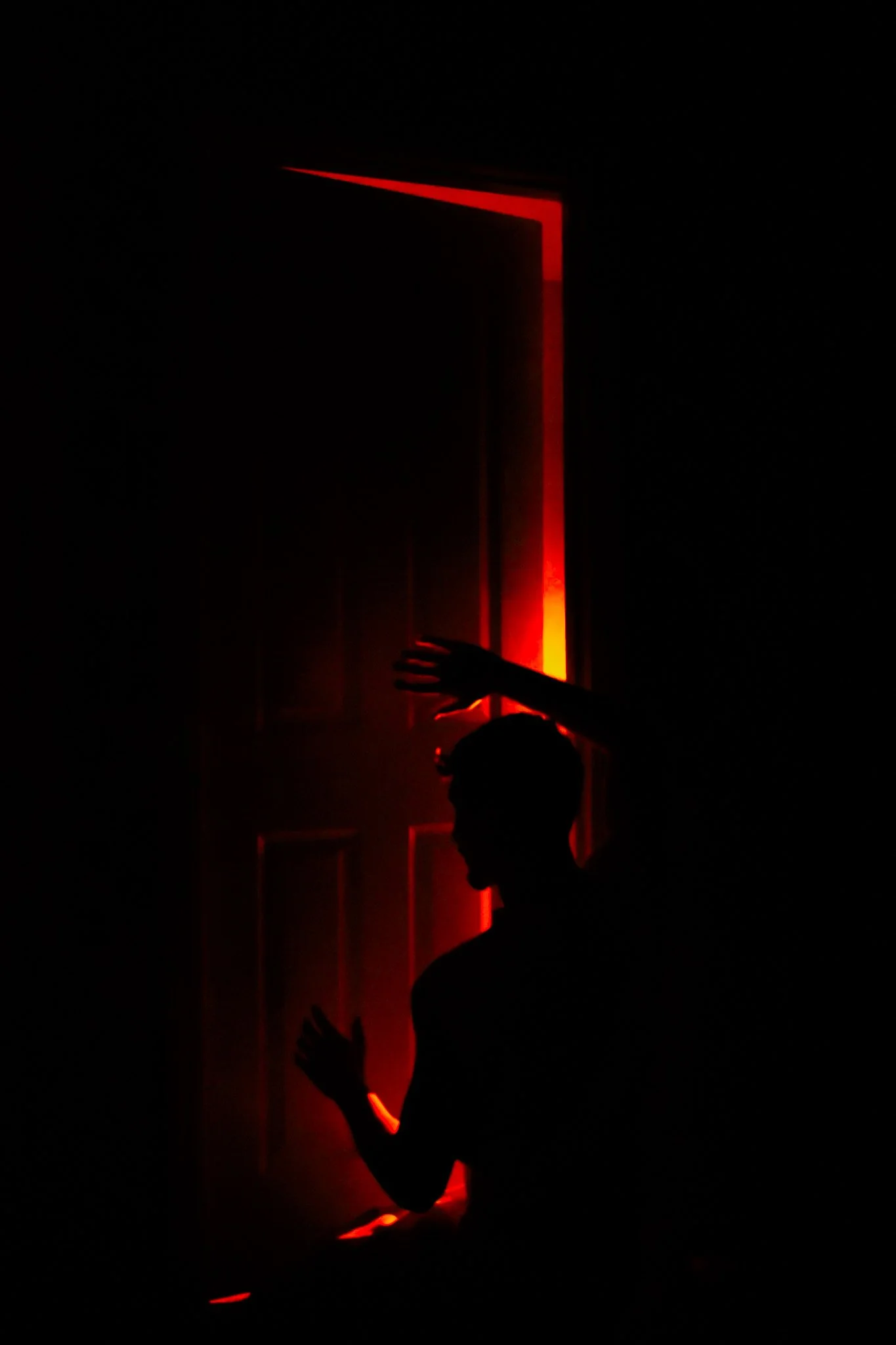 Silhouettes of children playing in a dark room with red glowing lines on the door.