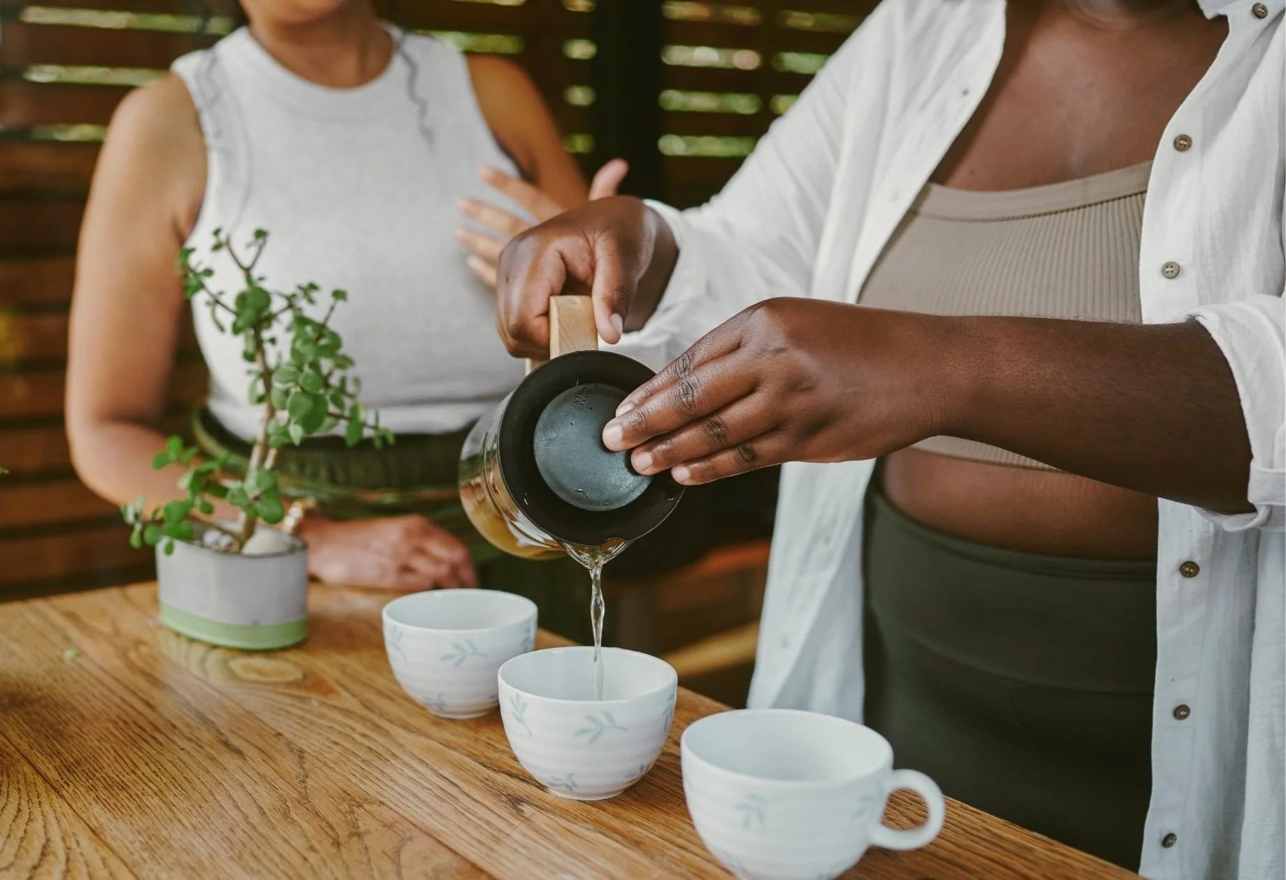 Woman preparing tea in a warm, welcoming setting, reflecting moments of connection, conversation, and community within a women's wellness space..