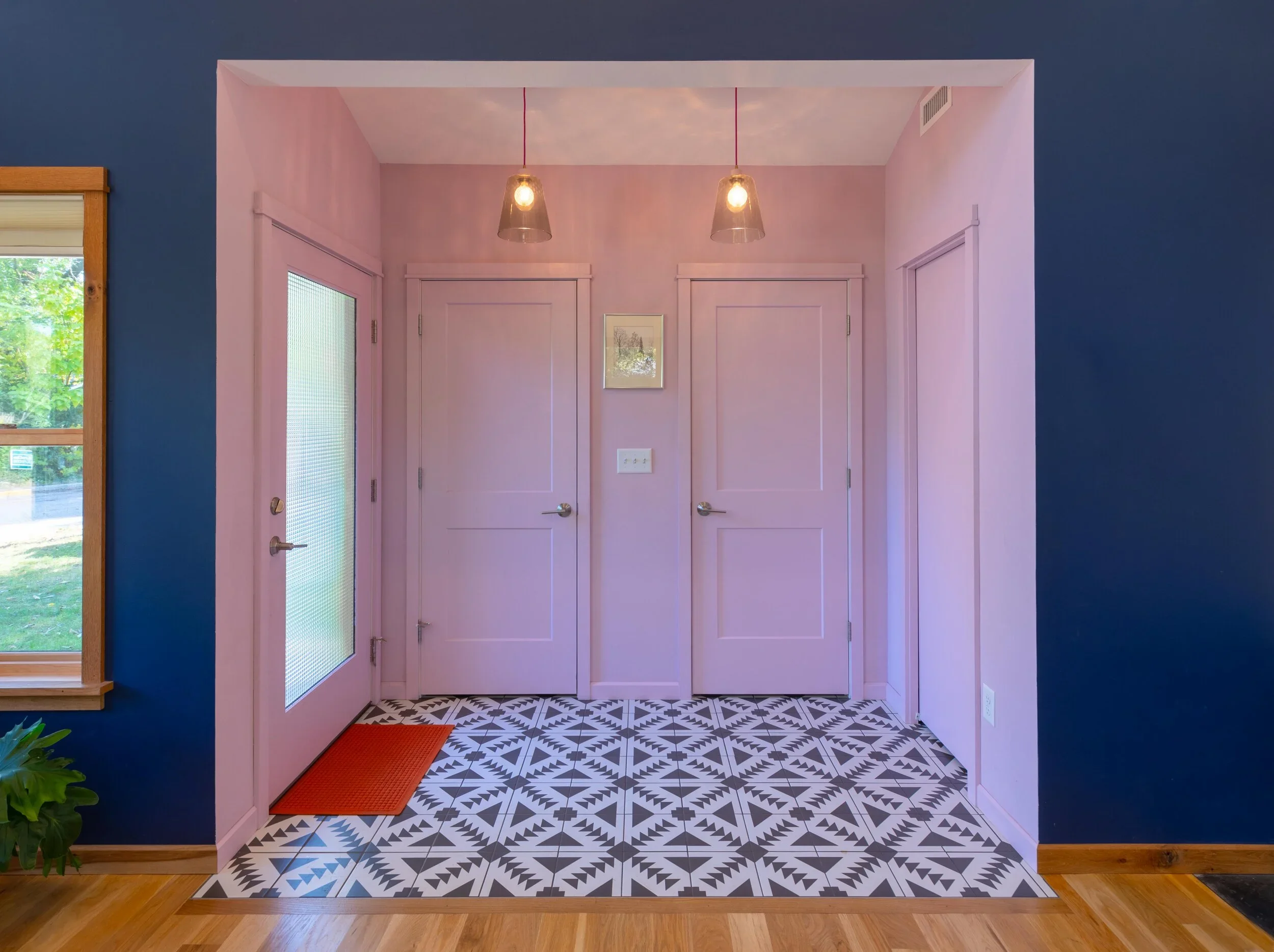 Entryway with pink walls, white door, patterned black and white tile floor, natural wood trim around window, and blue accent wall.