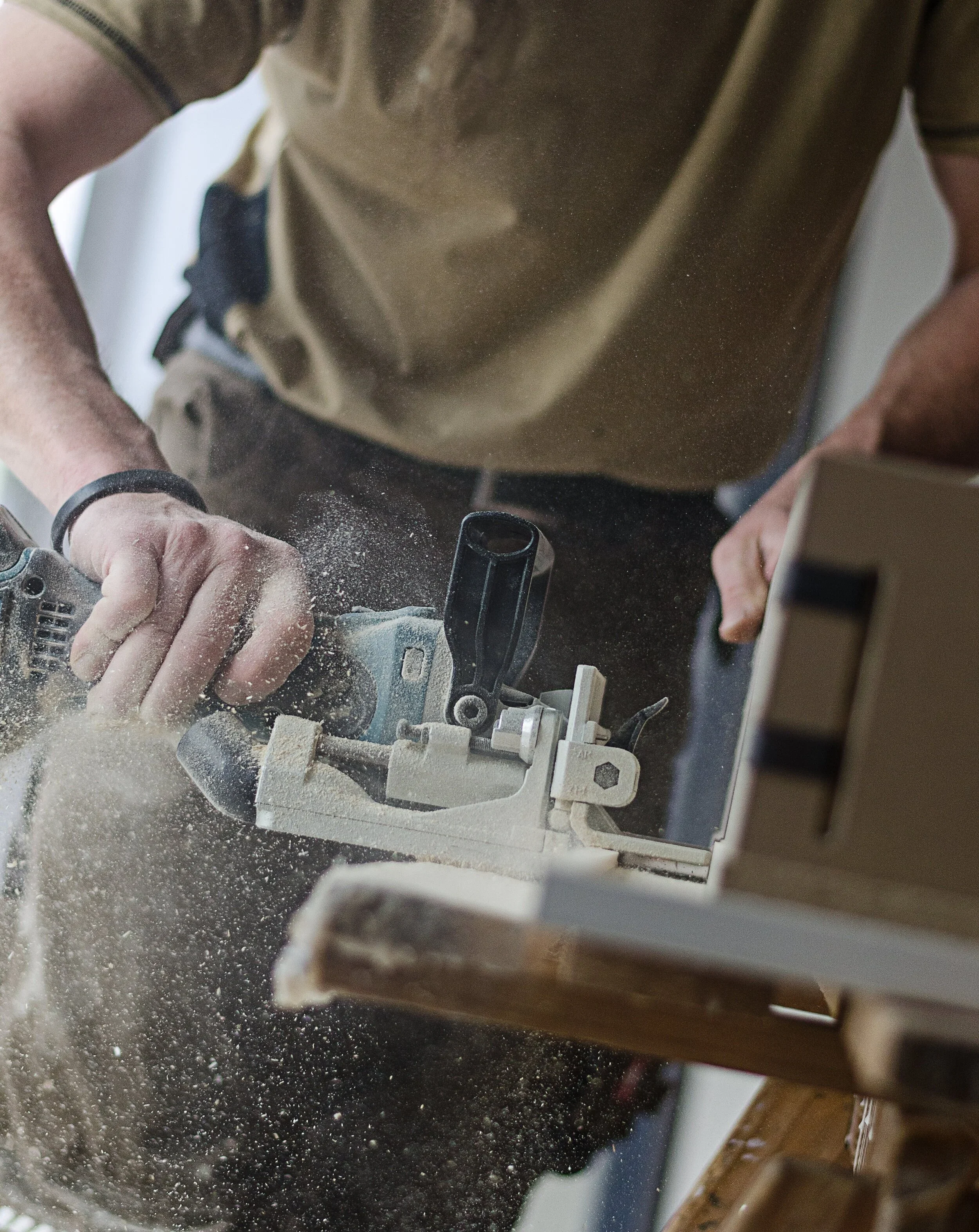 Person cutting wood with a power saw, wood dust in the air.