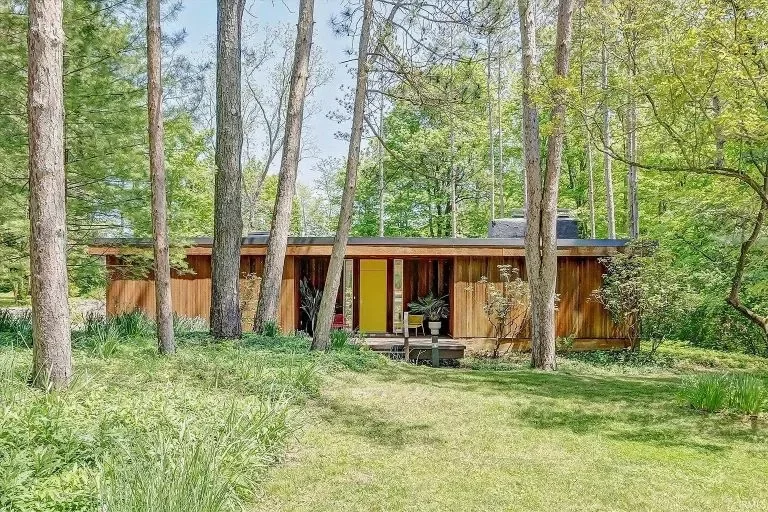 A modern, single-story house surrounded by trees with a grassy lawn in front.
