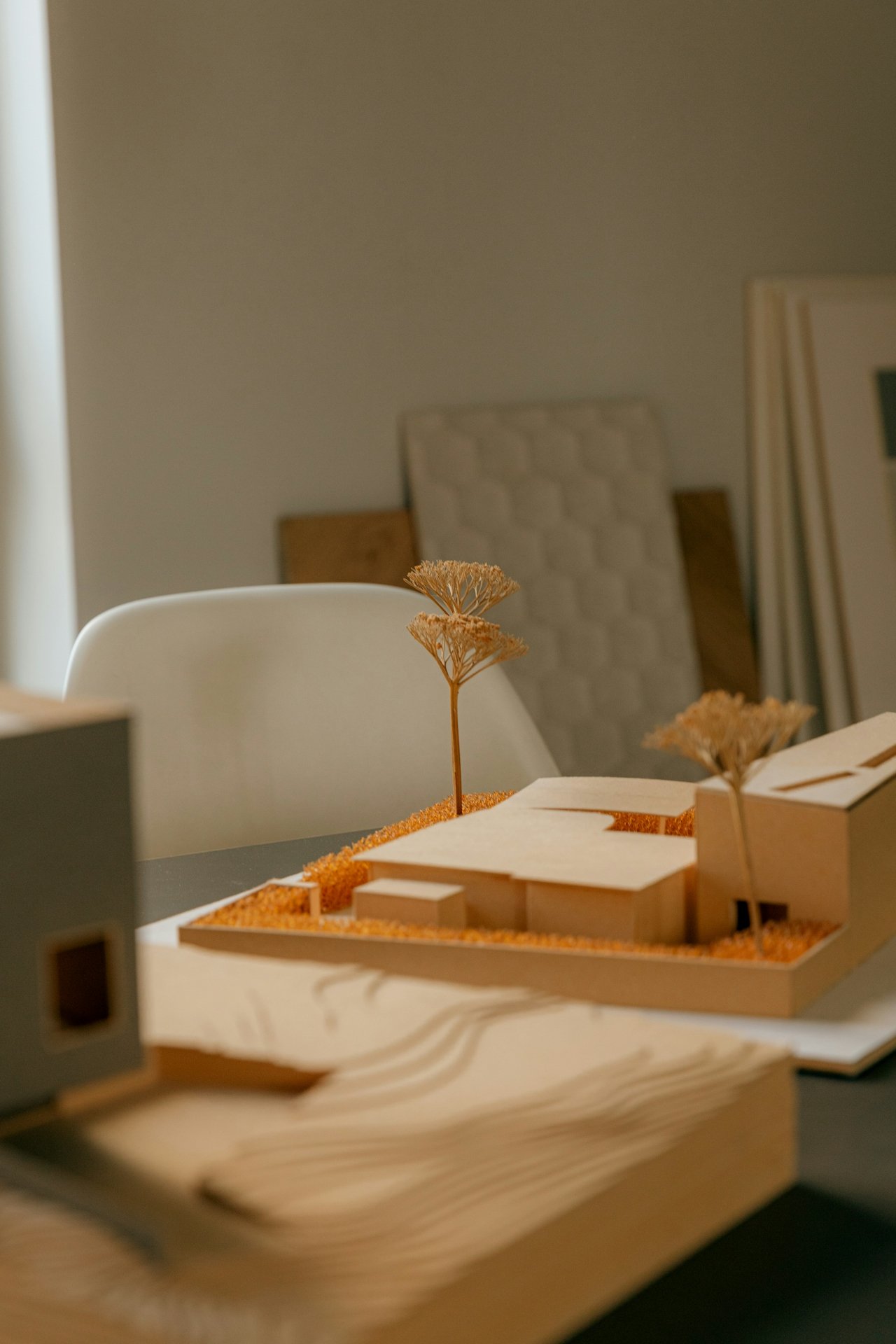 A detailed architectural model showcasing a building layout with trees, using wooden and paper elements placed on a table, with blurred background favoring focus on the model.
