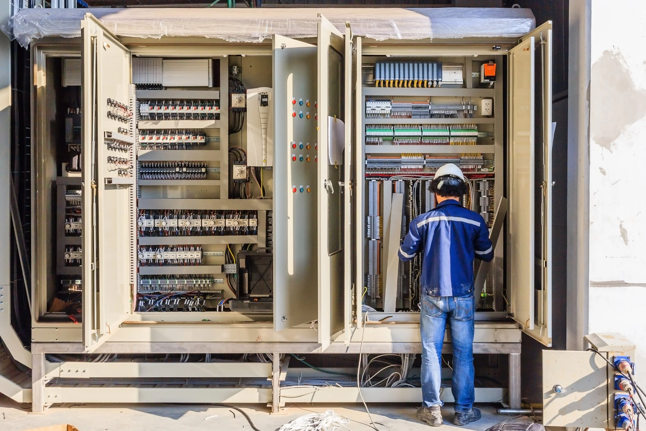 Man in blue shirt and a hard hat observing the PLC box