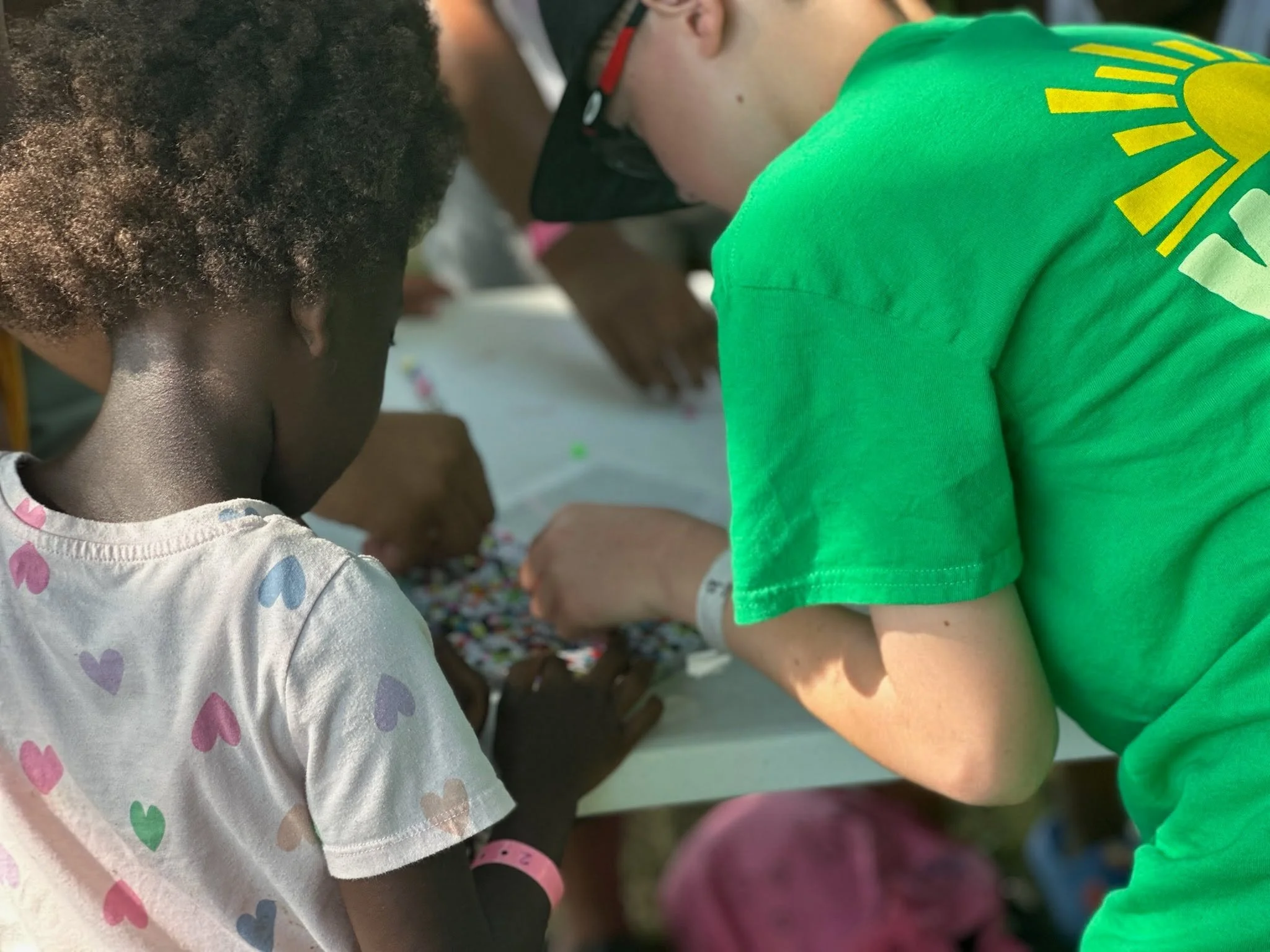 Close-up of children playing a game, wearing colorful clothing, with one child wearing a shirt with a yellow and green design and another wearing a shirt with pastel heart patterns.