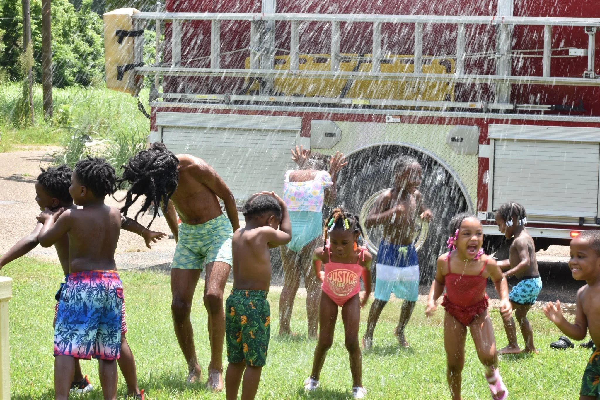 Children playing outside in the rain with a fire truck in the background.