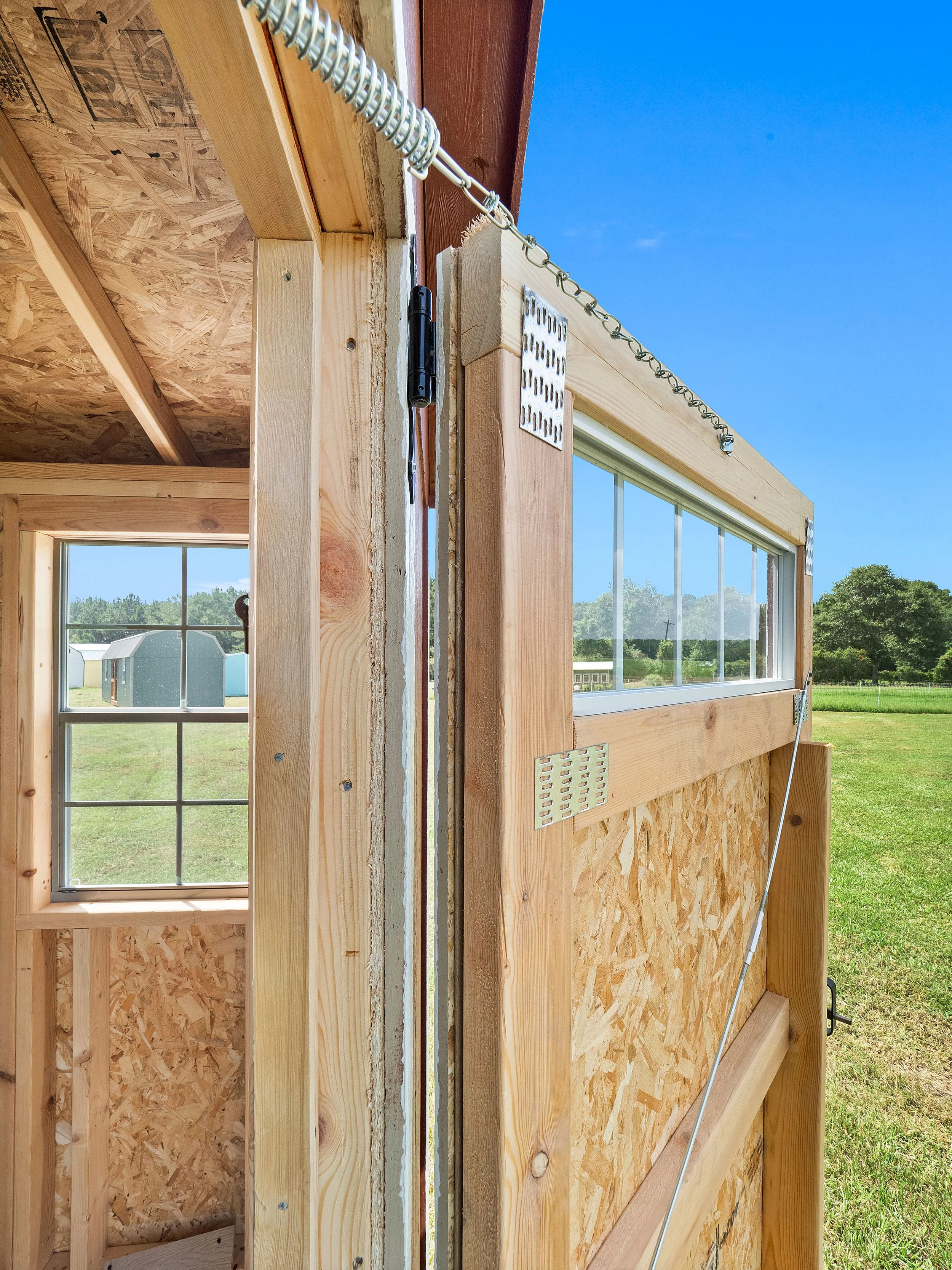 Close-up view of a door frame under construction, showing wooden framing, a chain, and a window with a rural landscape outside.