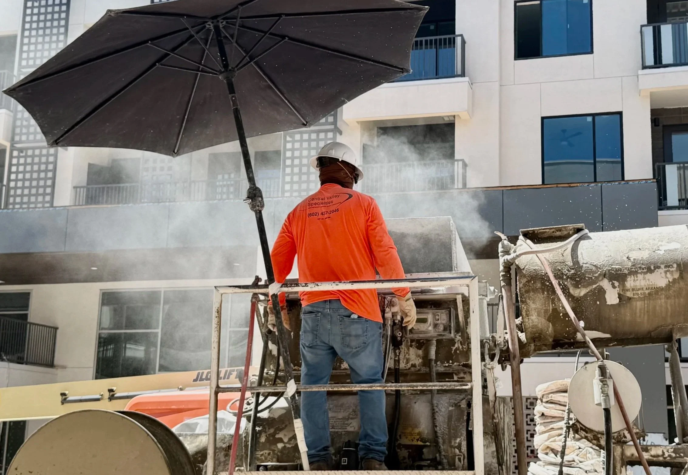 Construction worker in an orange shirt and white helmet operating a concrete mixer truck on a building site.