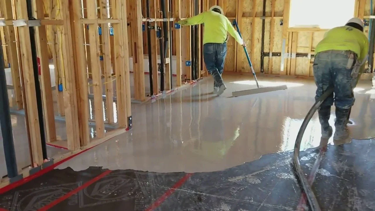 Construction workers pouring and smoothing concrete floor inside a building under construction.
