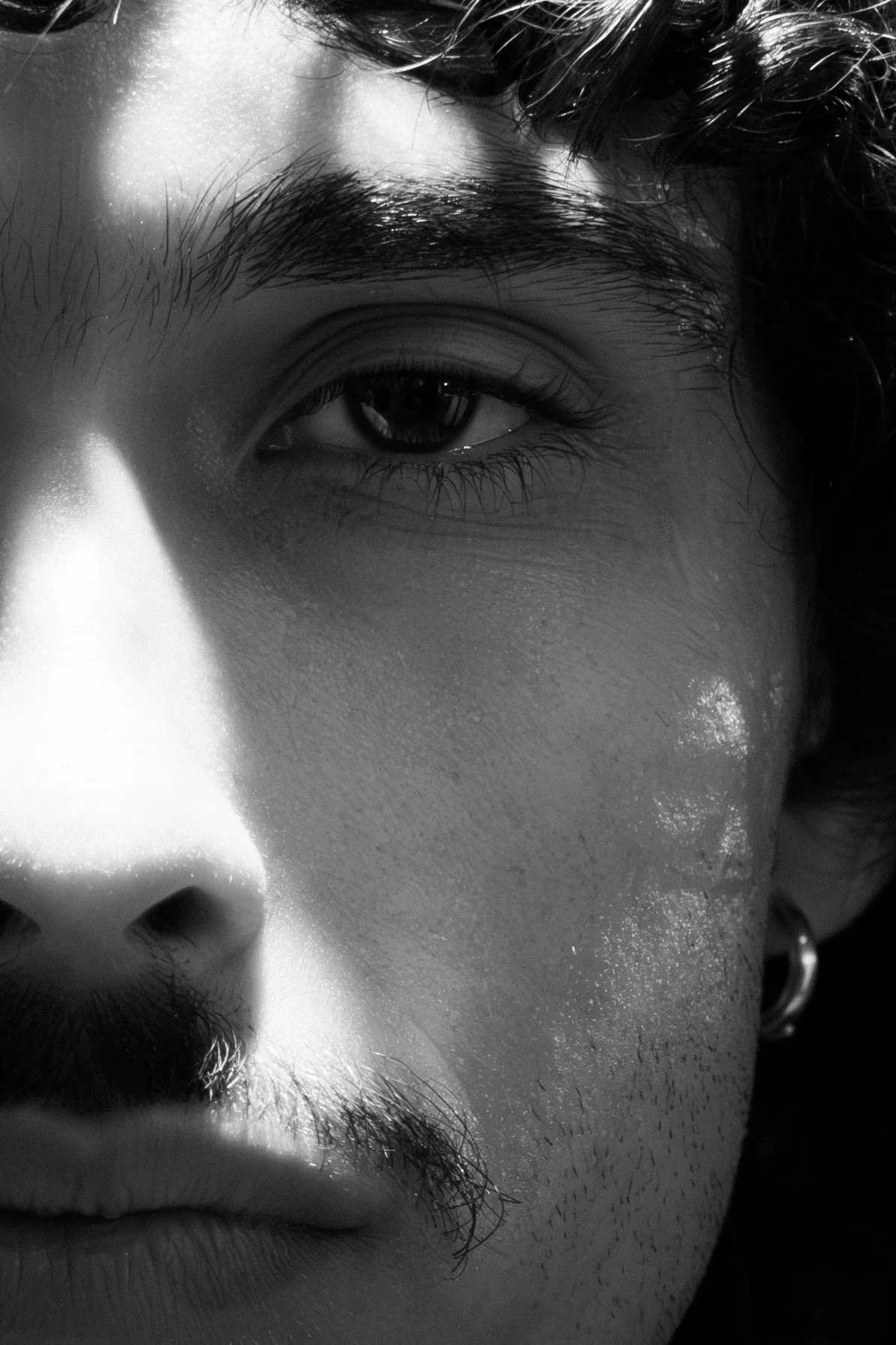 Close-up of a person's face focusing on the eye, eyebrows, and part of the nose, in black and white.