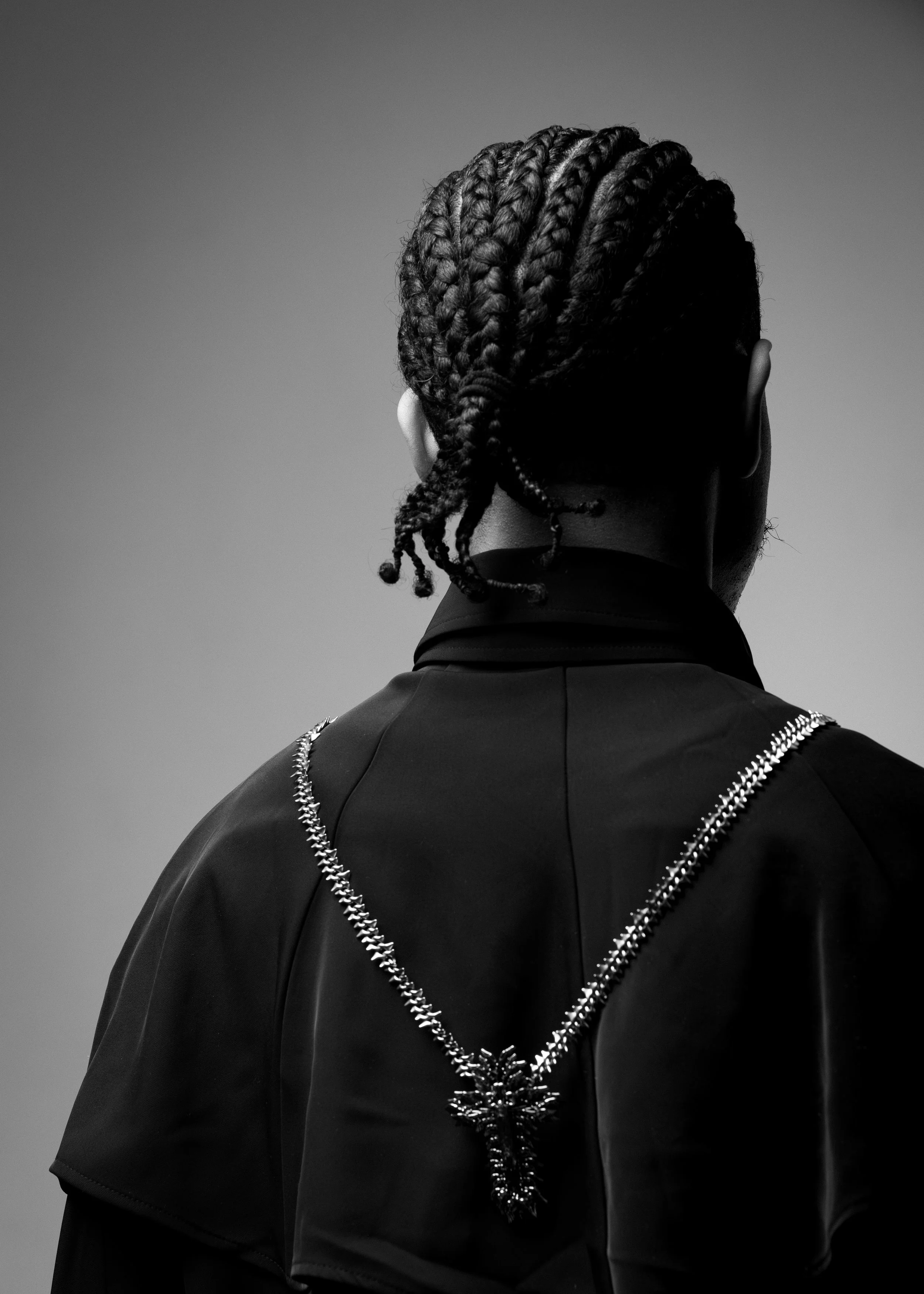 Back of a woman with braided hair wearing a dark outfit with a star-shaped necklace.