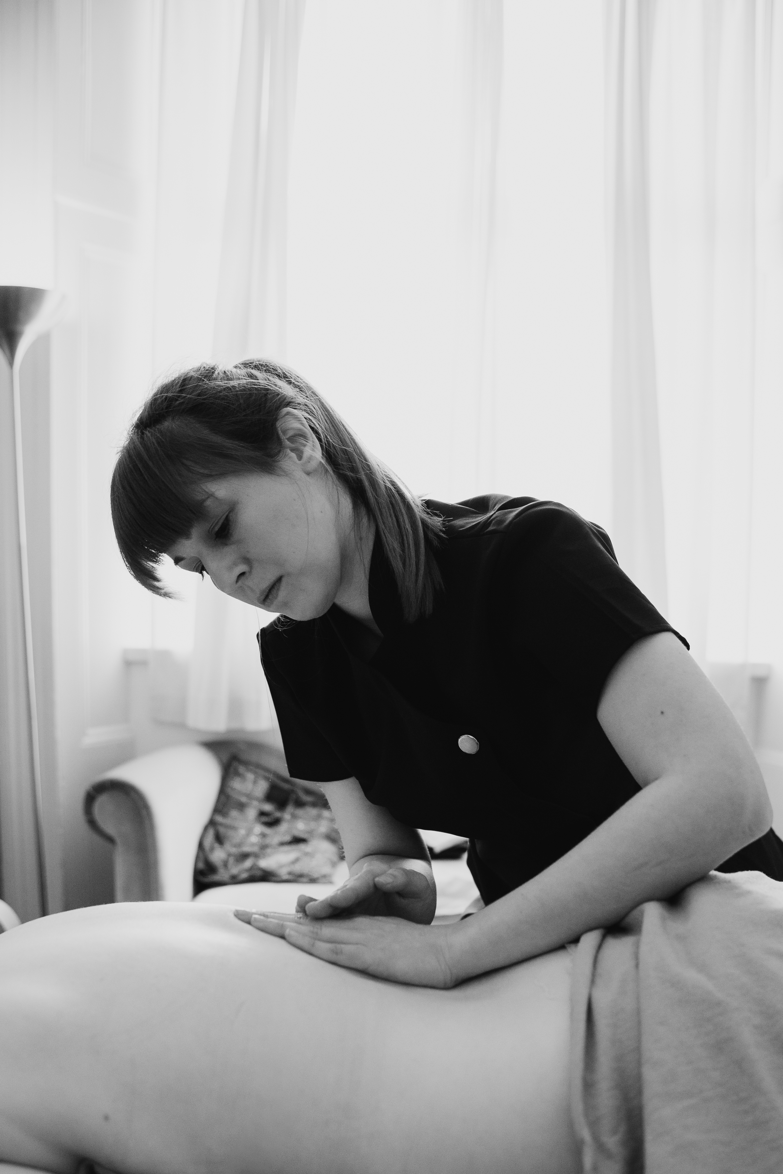 A woman giving a massage or therapy to a person's back, indoors with white curtains in the background.