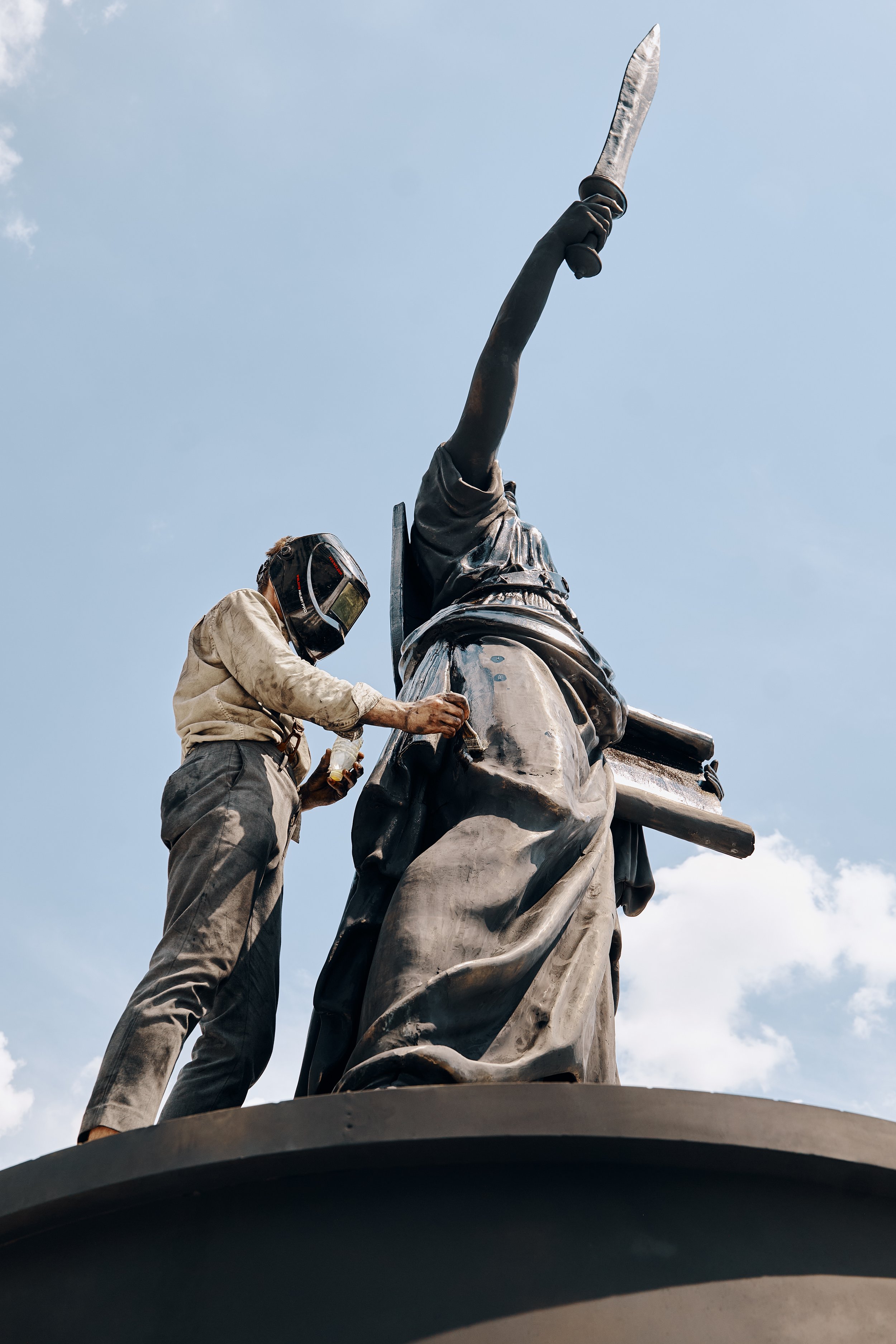 Worker in protective gear cleaning or repairing the Statue of Liberty.