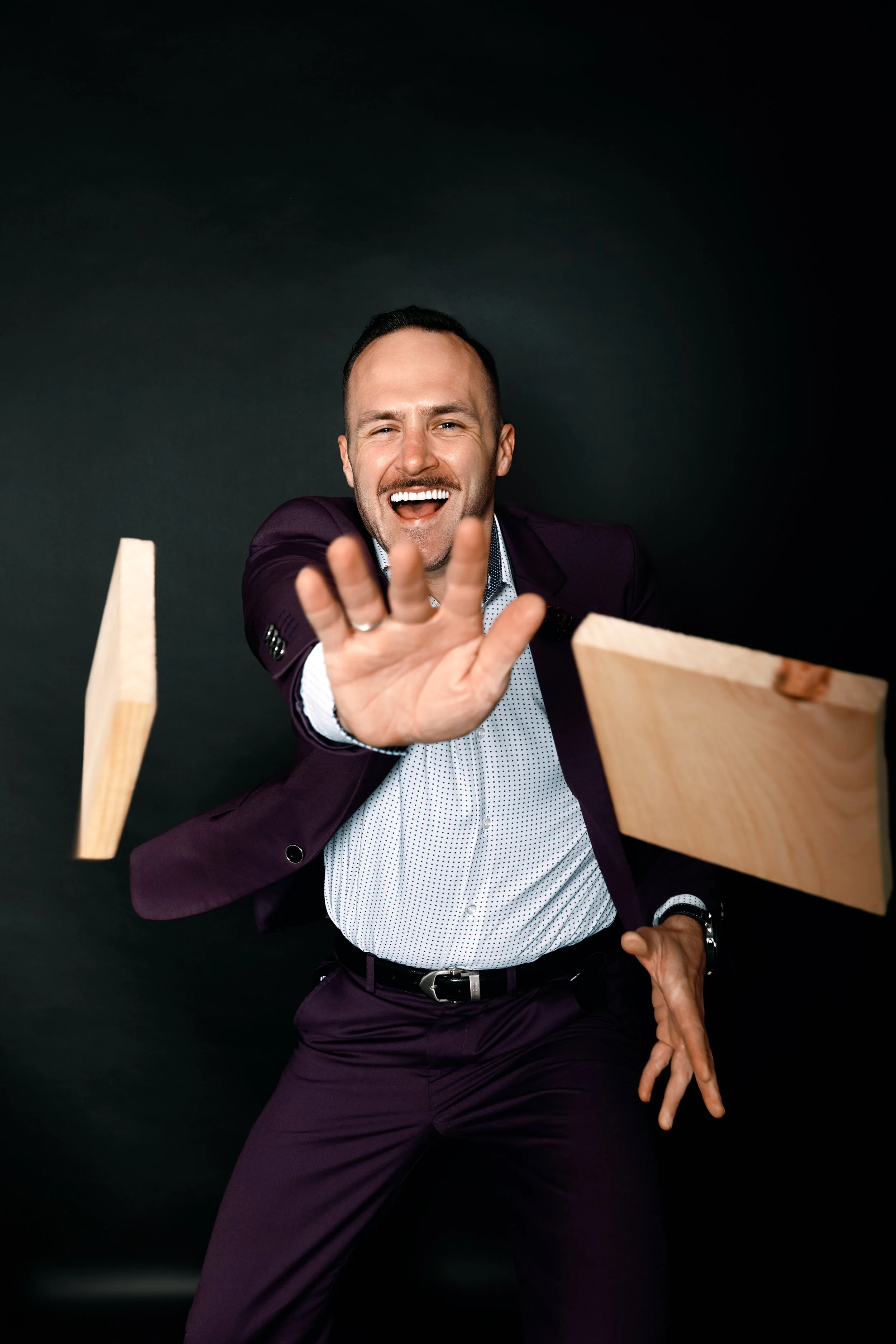 A man, Front Row Frankie, in a purple suit reaching forward with both hands, laughing, against a dark background.