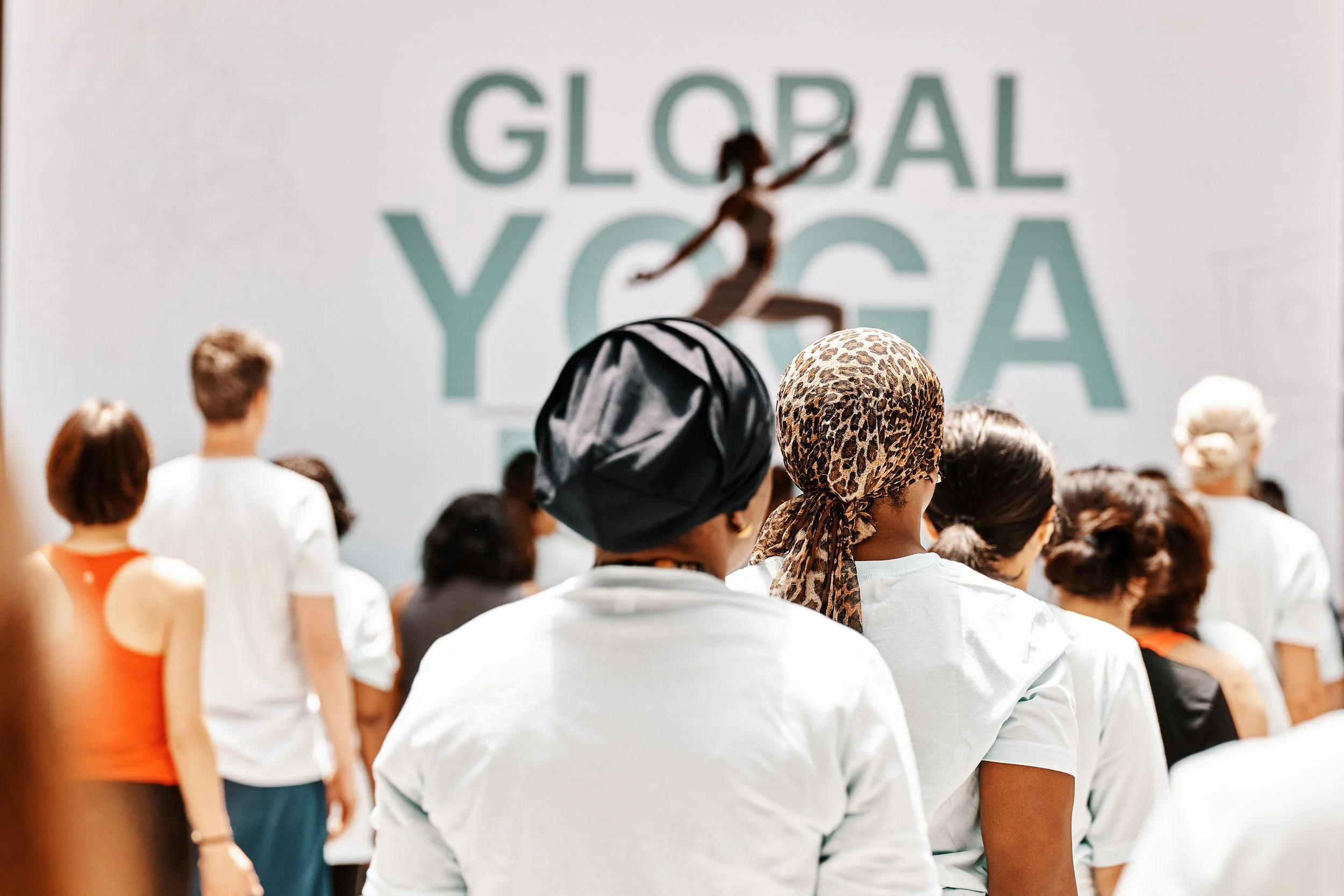 Crowd of people attending a yoga event with a backdrop displaying the words 'Global Yoga' and an image of a person practicing yoga.