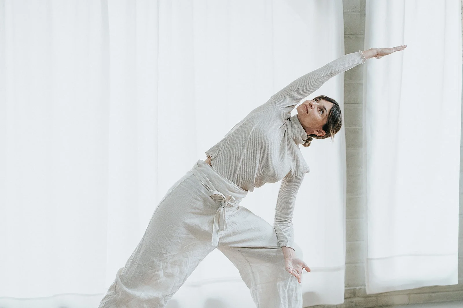 Una donna che fa esercizi di stretching in una stanza luminosa con tende bianche.