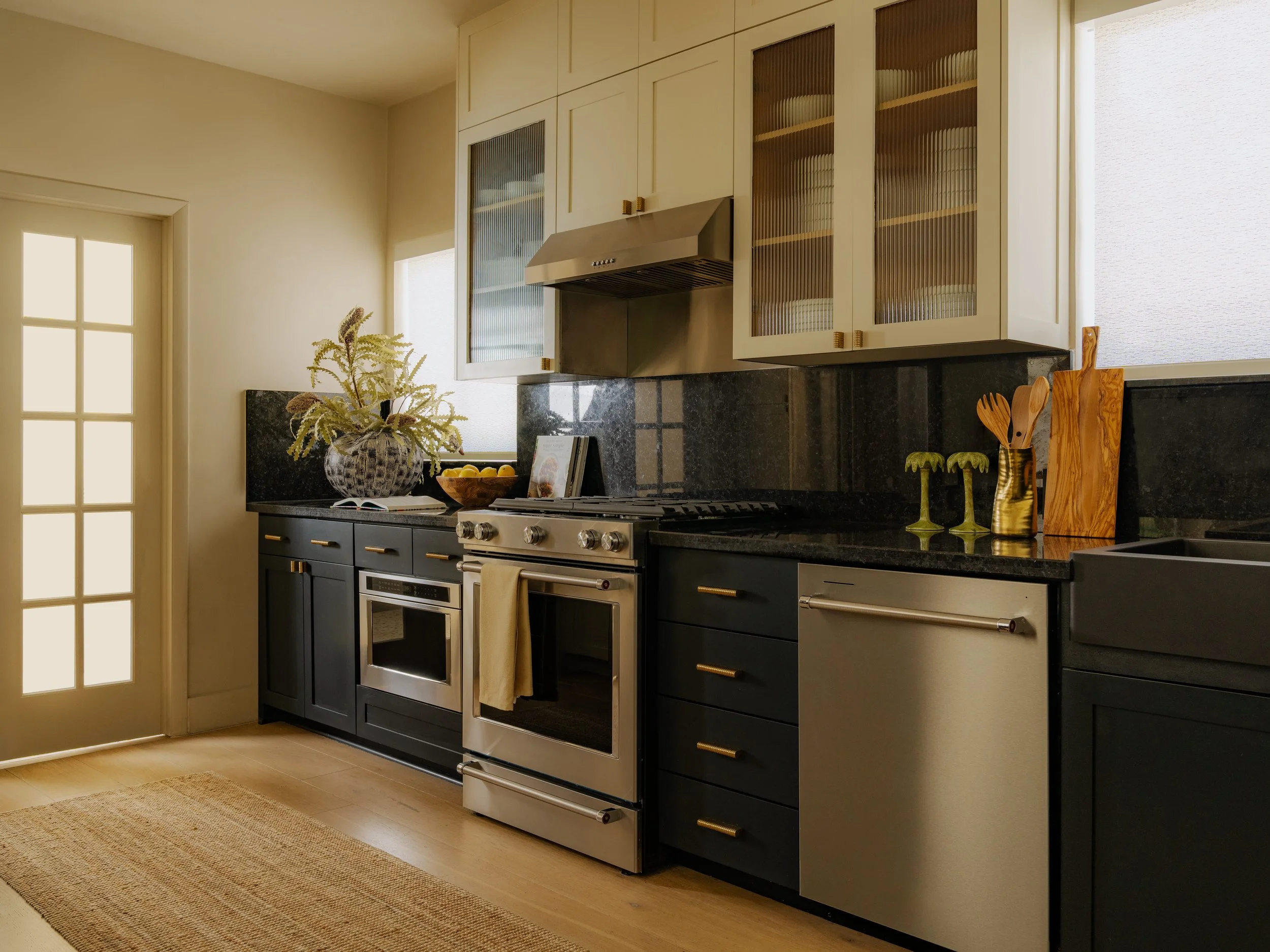A modern kitchen with dark cabinets, a stainless steel stove and hood, decorative vases, and a window with frosted glass next to a closed door.