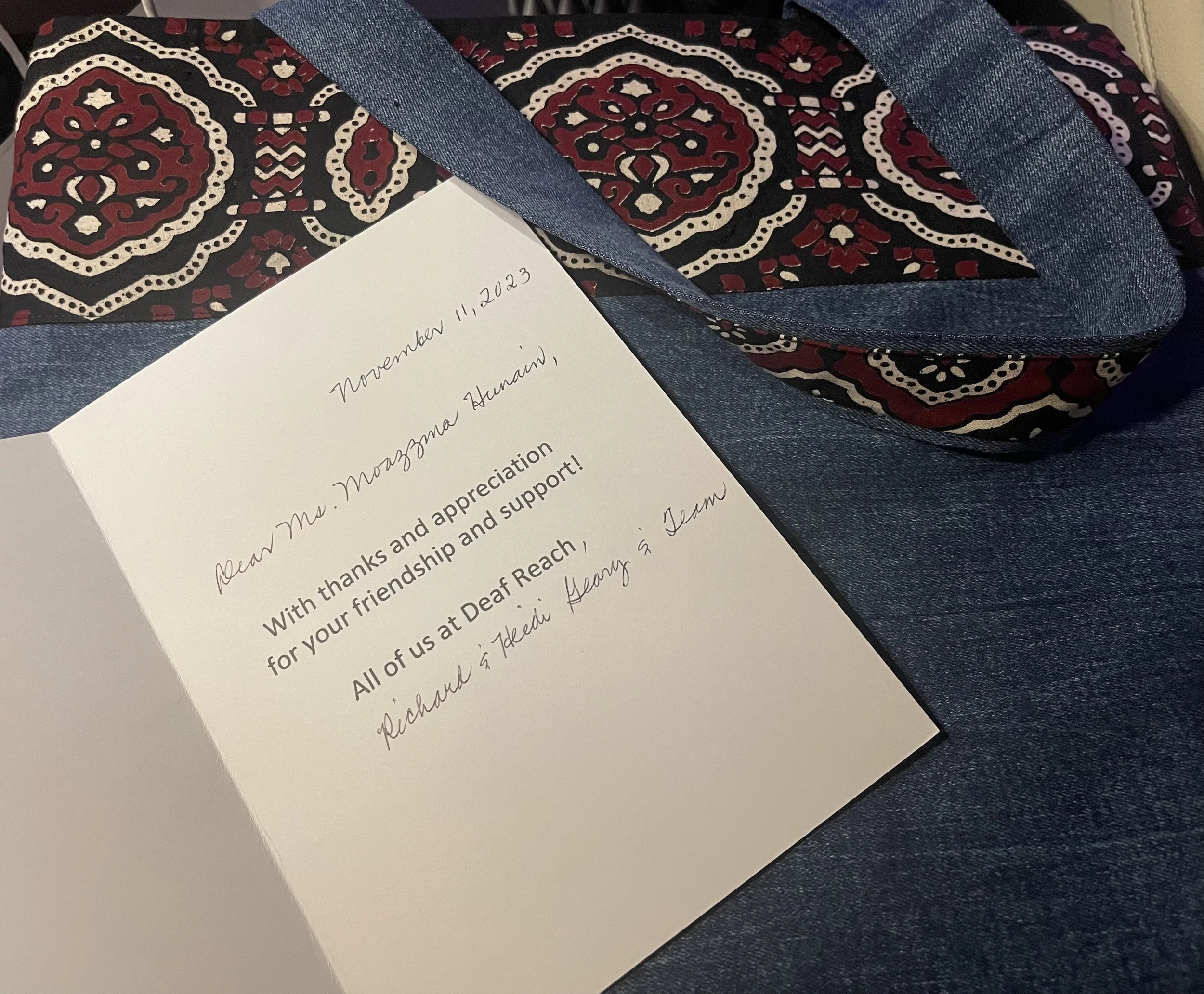 A thank you card with handwritten message inside, resting on a patterned scarf with red and white designs, and blue denim fabric underneath. Moazzma Hunain Foundation receives thank you letter from Deaf Reach, Pakistan