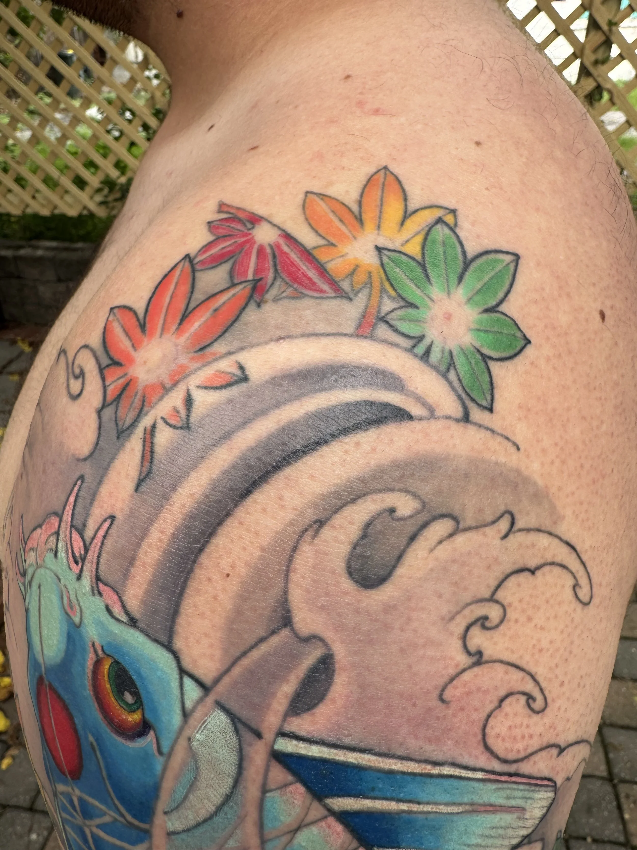 Colorful tattoo featuring flowers and a wave pattern on a person's upper arm.