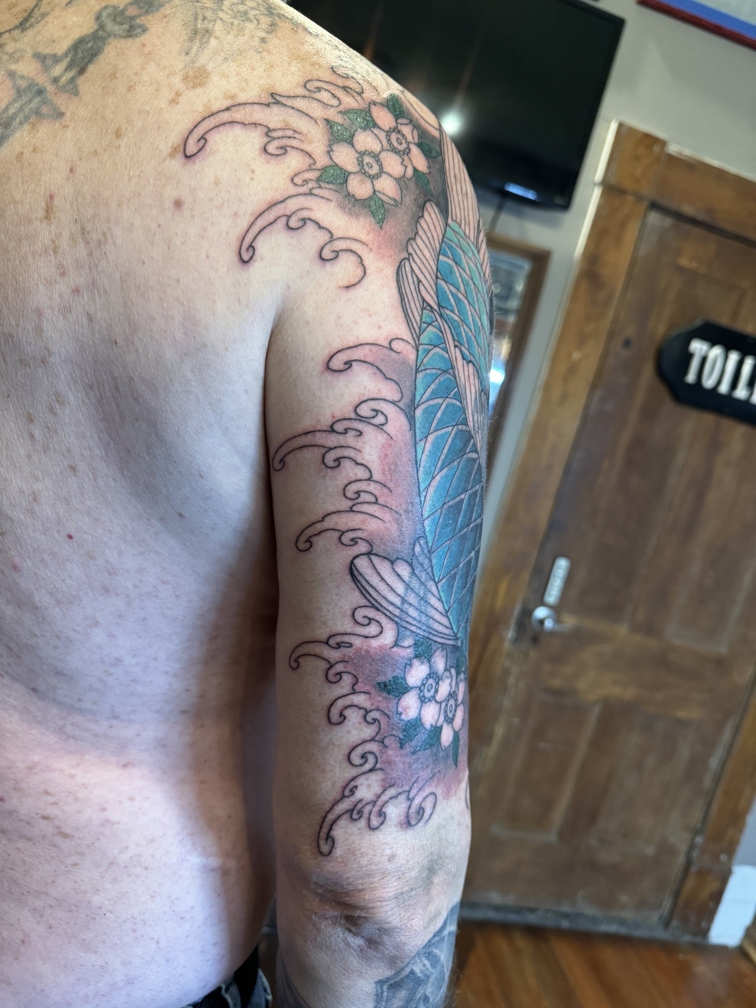Tattoo of waves, flowers, and colors on a person's arm.