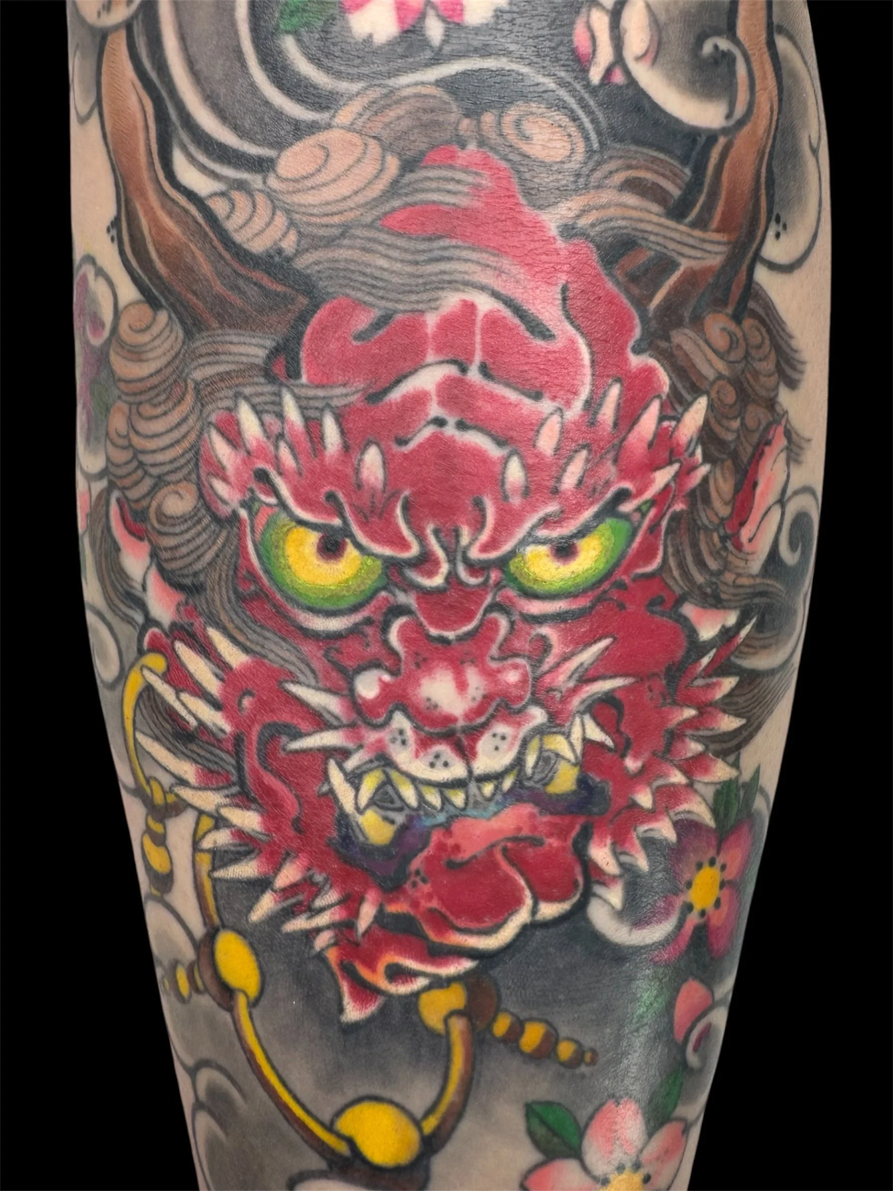 A traditional Japanese Hannya mask tattoo with vivid colors and detailed linework on skin, featuring a fierce expression, yellow eyes, red and black details, and surrounded by cherry blossom flowers.