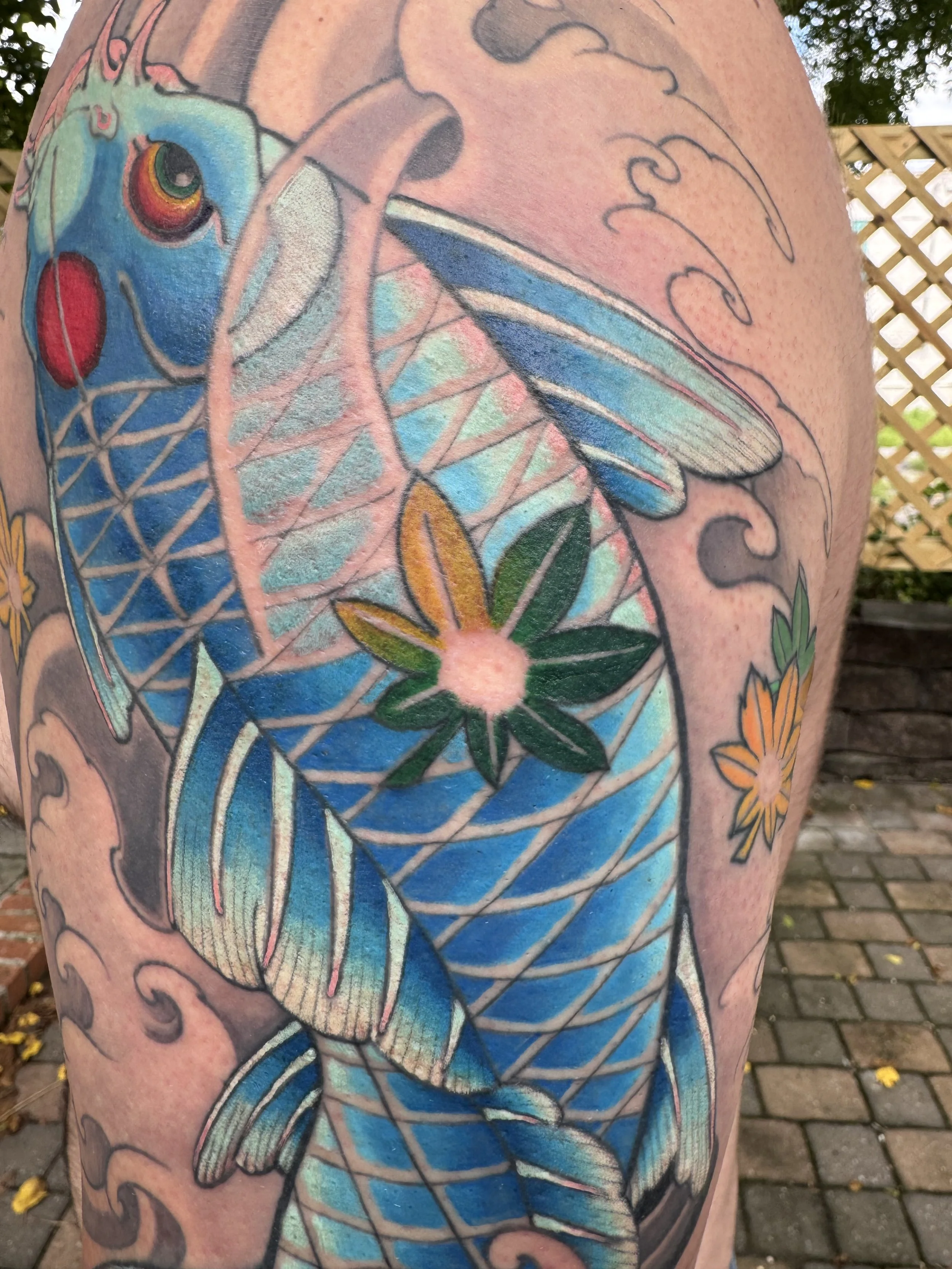 Close-up of a colorful tattoo of a fish with detailed scales, fins, and a large eye, on a person's arm.