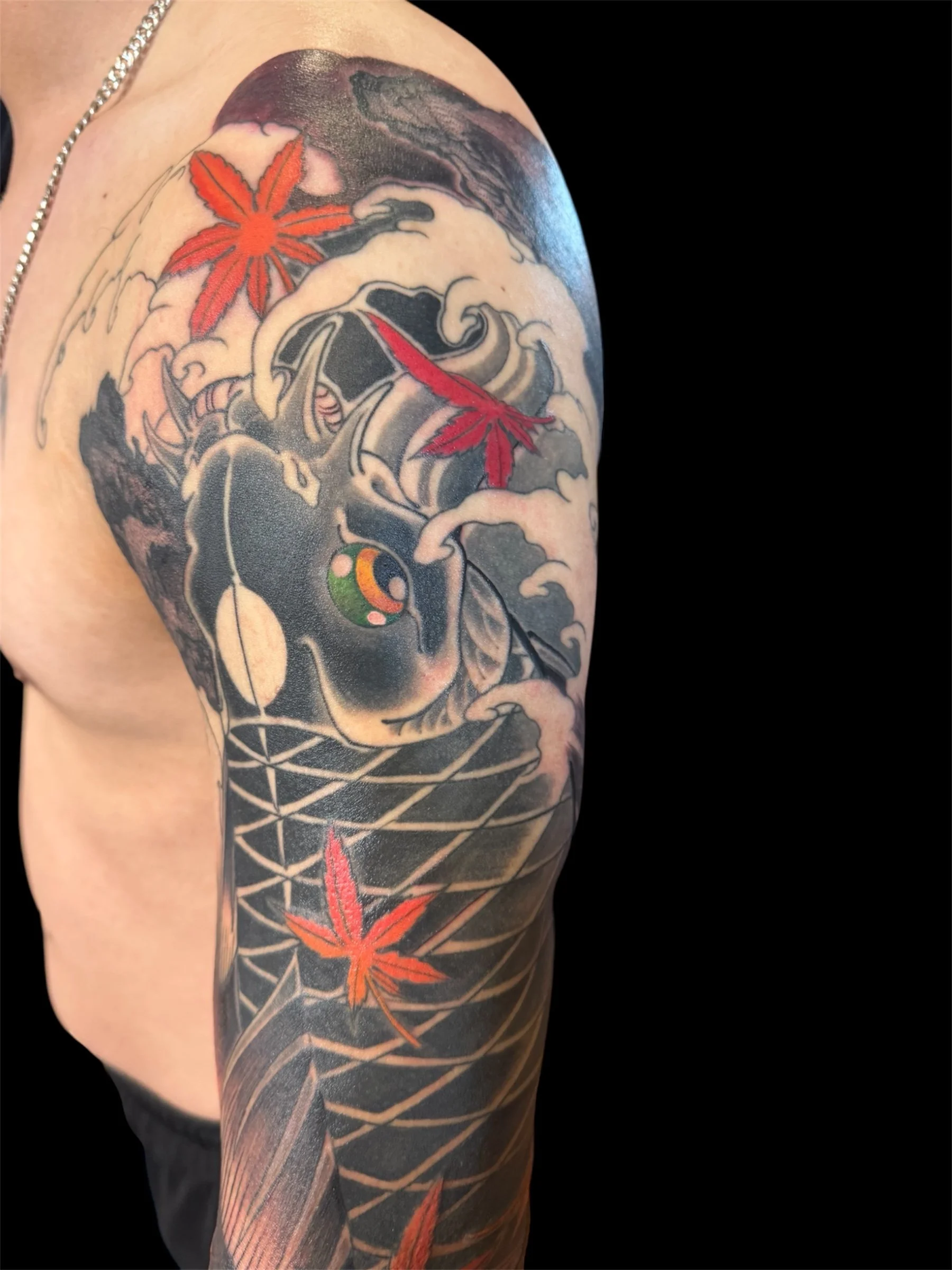 Tattoo sleeve on person's upper arm featuring a traditional style black dragon, red maple leaves, clouds, and geometric patterns.