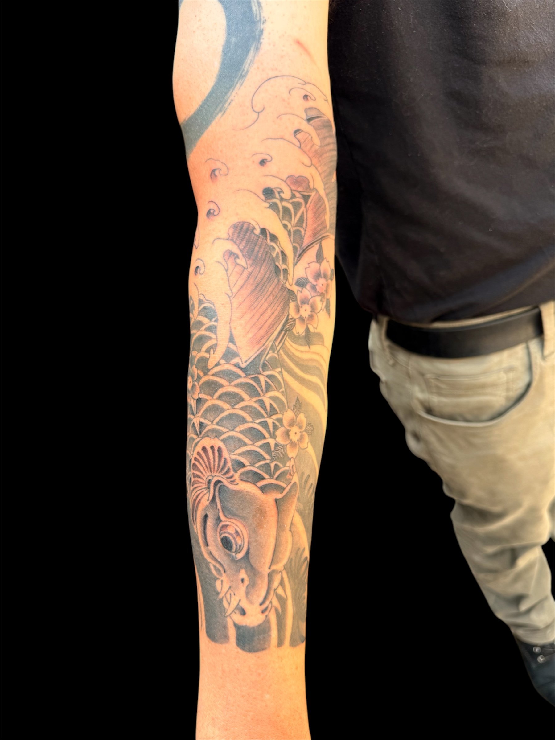 A tattoo sleeve featuring Japanese waves, a koi fish, cherry blossoms, and traditional Japanese motifs.