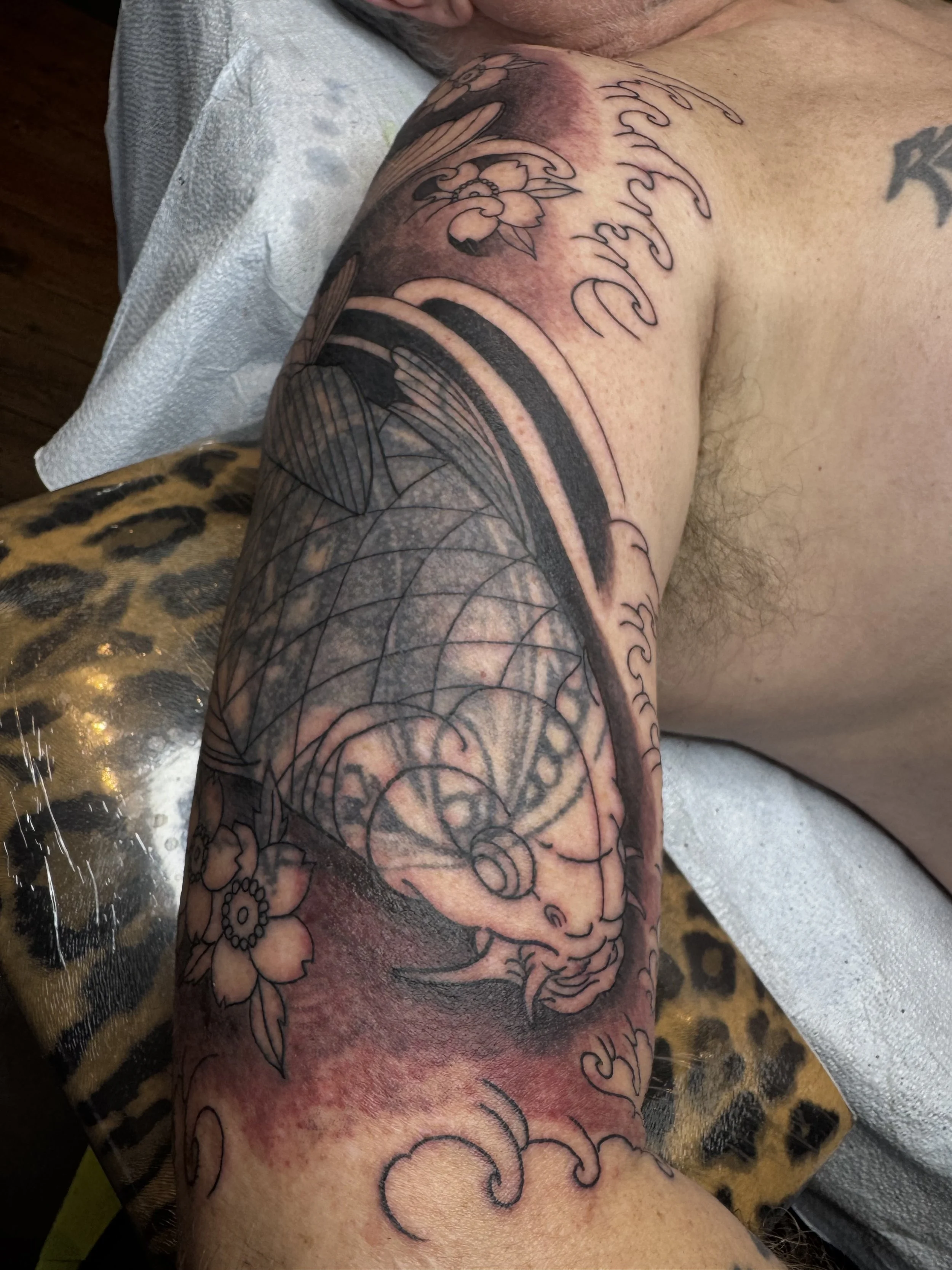 A person's arm with a partially completed tattoo, including floral and geometric designs, and some text.