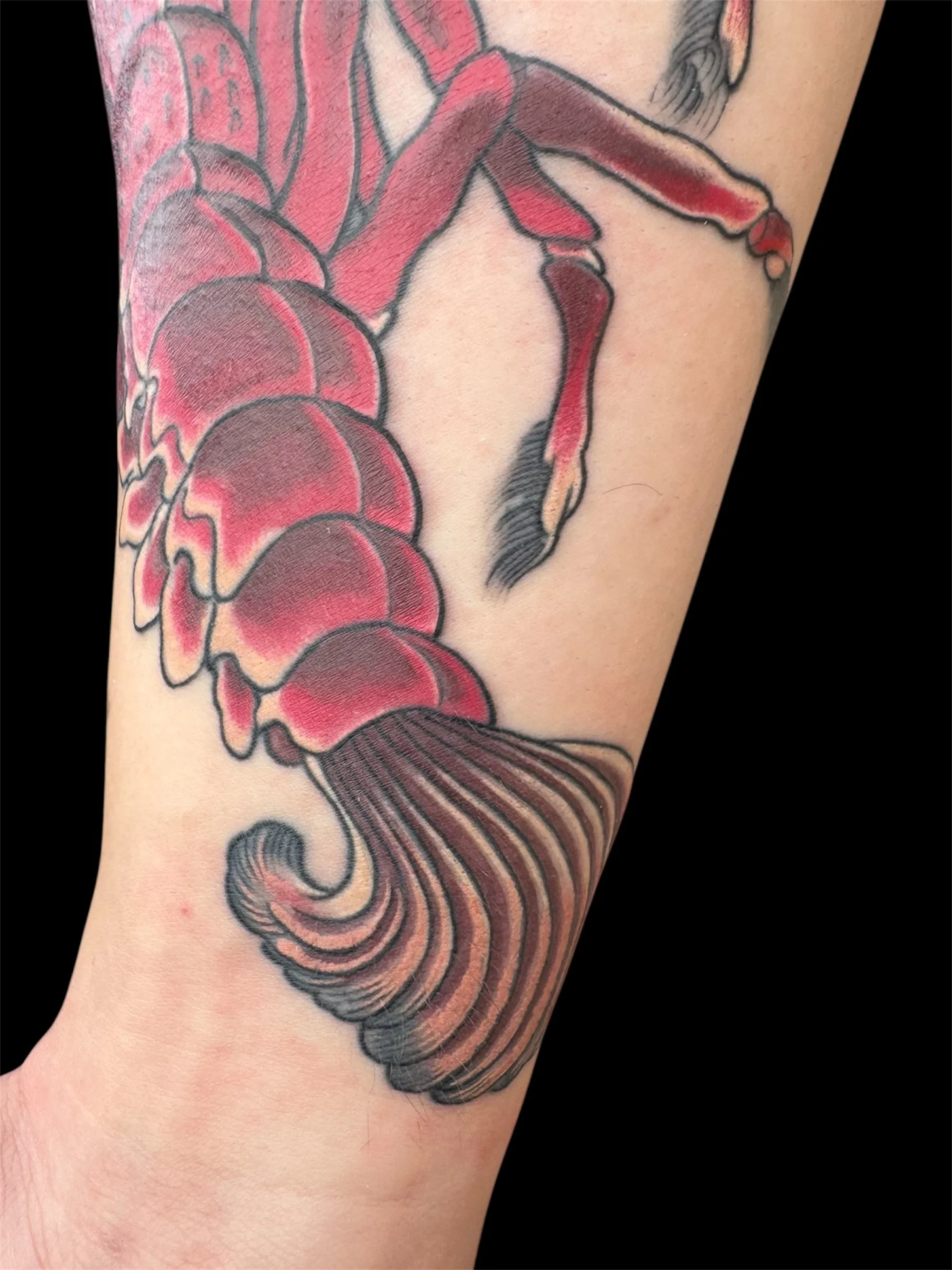 Close-up of a tattoo on a person's arm, depicting a traditional style fish with red and black ink details.