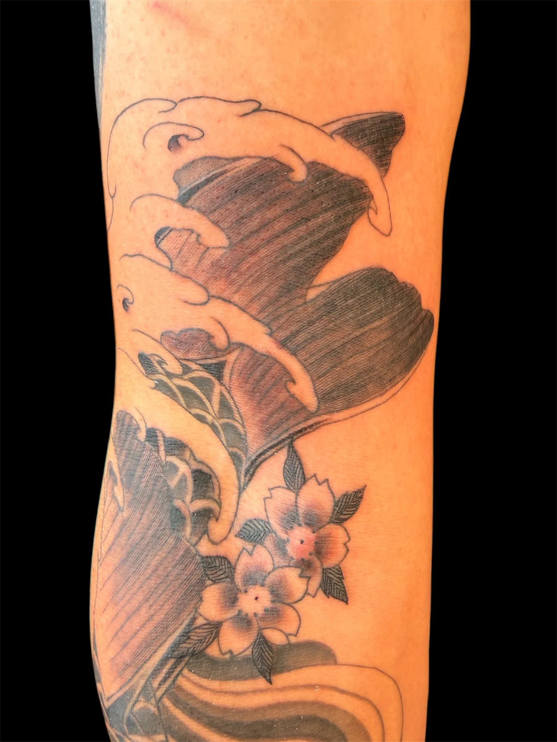 Close-up image of a tattoo on skin, featuring a large, detailed flower with petals, leaves, and shading.