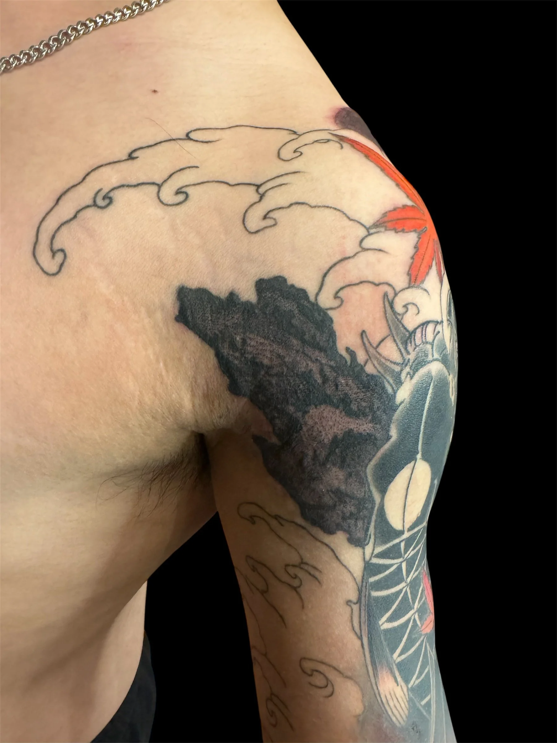 Close-up of a person's shoulder and upper arm with a tattoo of stylized waves and a fish, with some red detailing on the fish's fins.