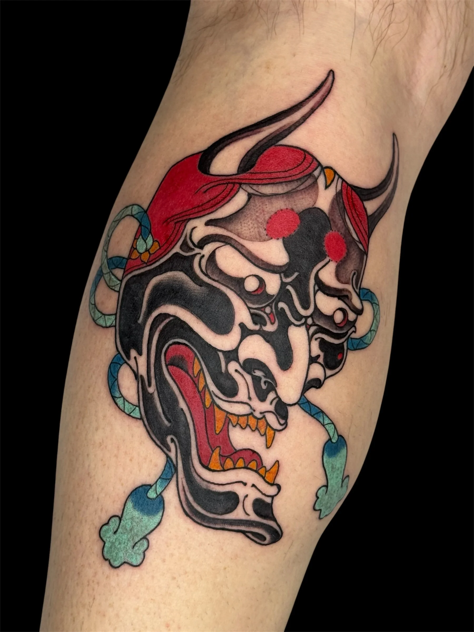 Tattoo of a traditional-style playing card with a skull, red hair, and ribbons on a person's arm.