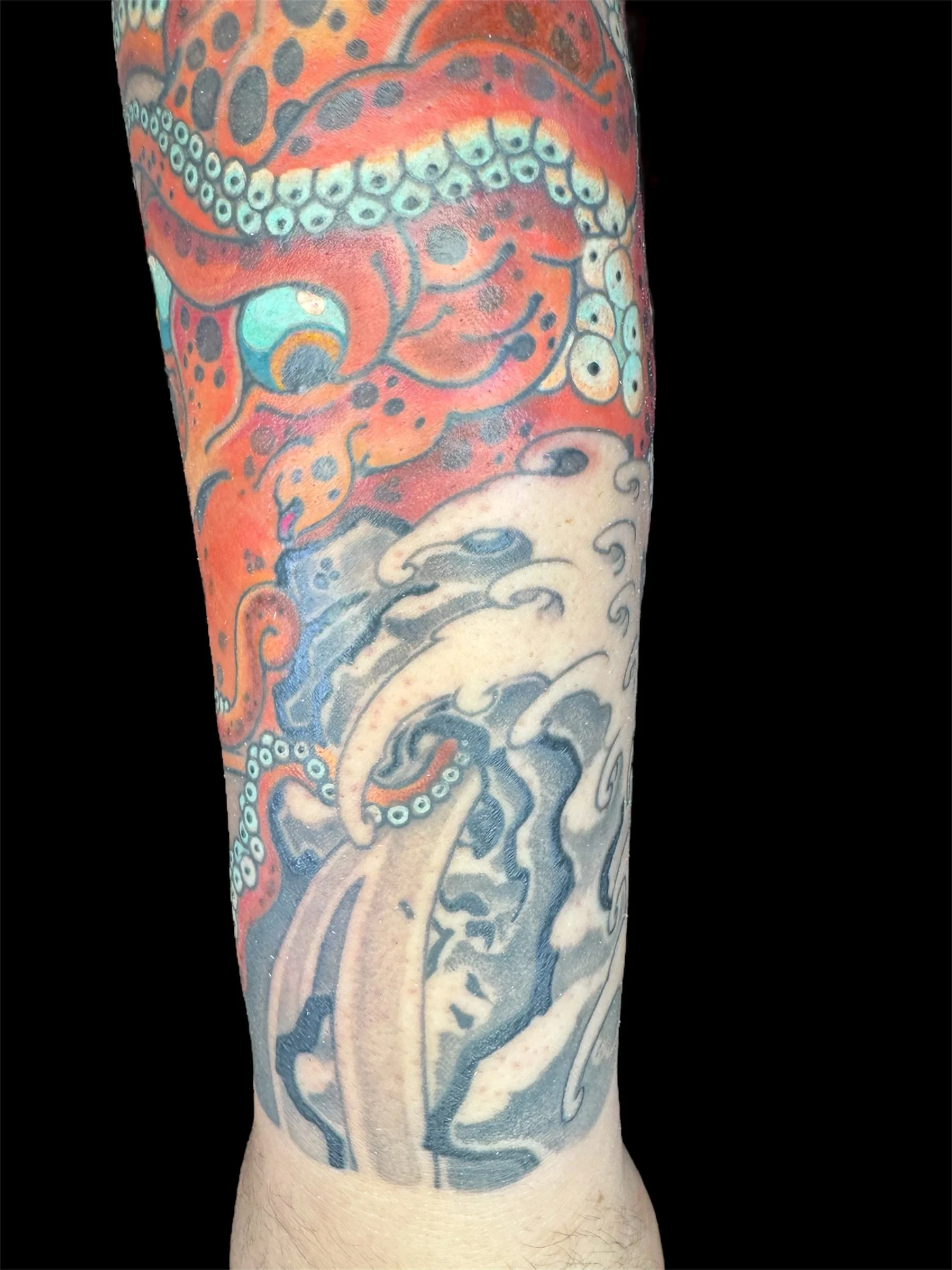 Close-up of a tattoo on a person's arm, featuring vibrant colors and intricate designs including swirling patterns and possibly an octopus with tentacles.
