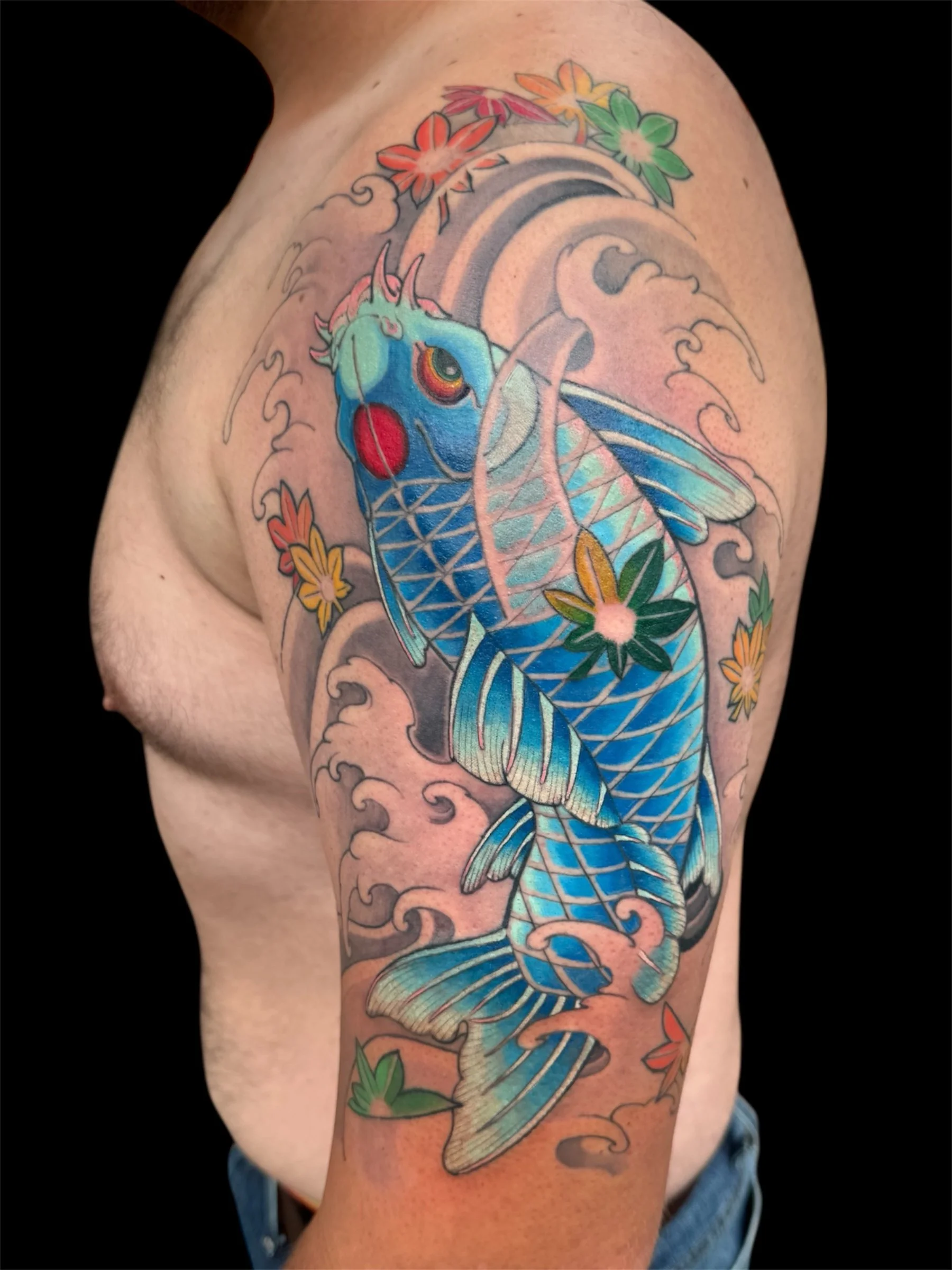 A colorful tattoo of a koi fish swimming in water, surrounded by flowers and waves on a person's upper arm.