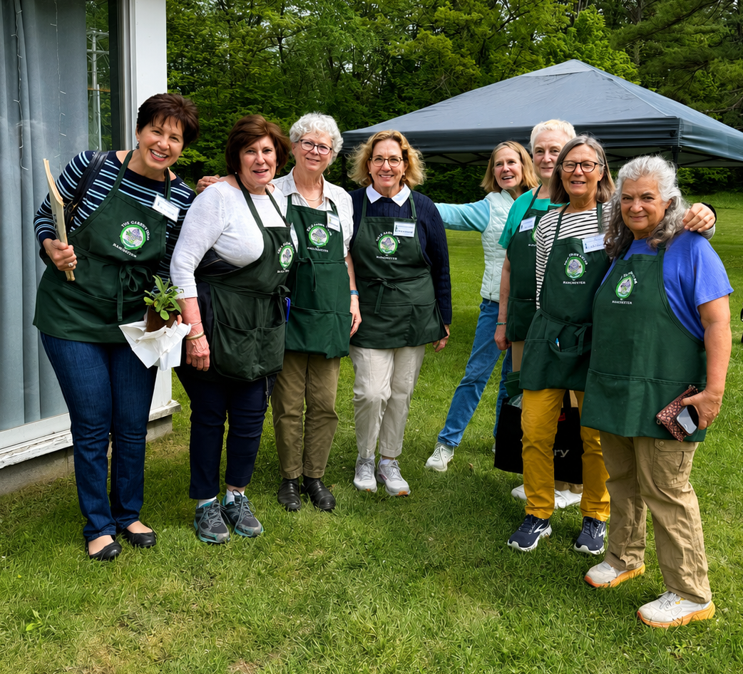 Group of women standing outdoors, wearing green aprons with a logo, posing for a photo during a gardening event.