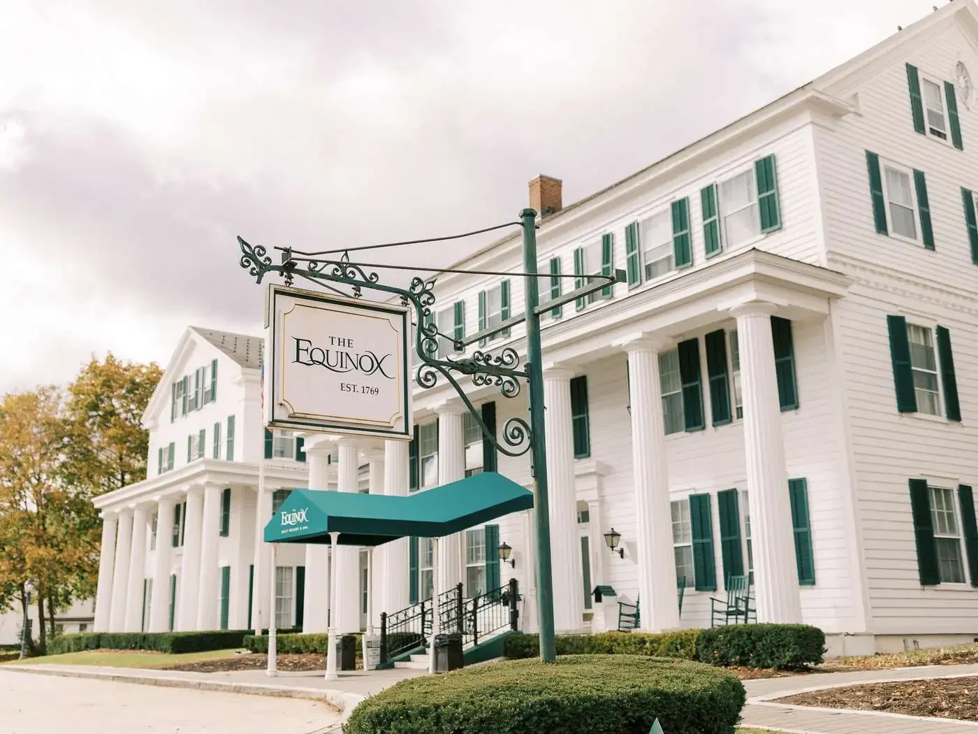 White multi-story building with green shutters, columns at the entrance, and an outdoor sign that reads "The Equinox, Est. 1769" under a teal canopy.