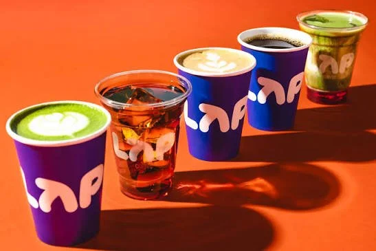 Five colorful cups with various beverages on an orange surface, casting shadows.