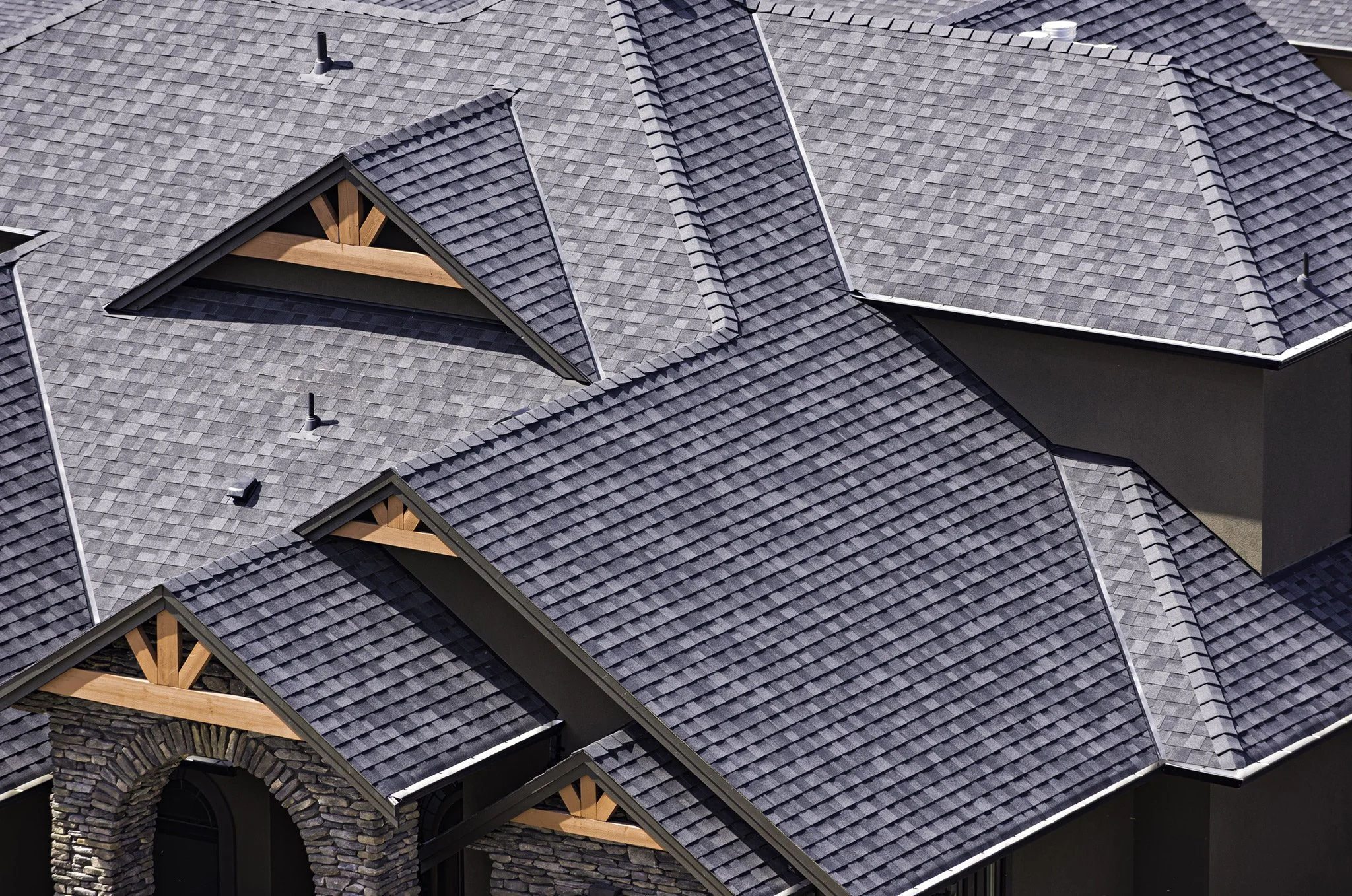 Aerial view of a house with multiple gray shingled roofs, dormer windows, and a stone facade over the entrance.