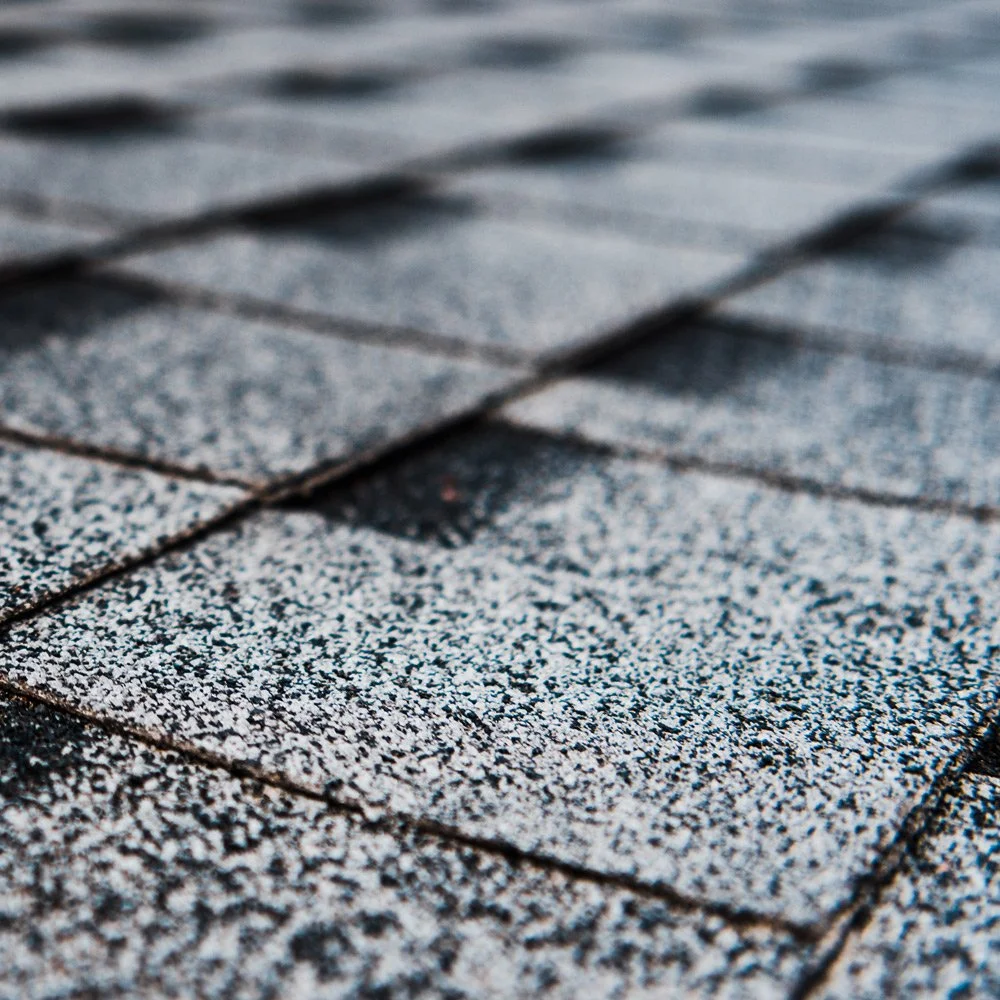 Close-up of asphalt shingles dusted with snow on a roof.