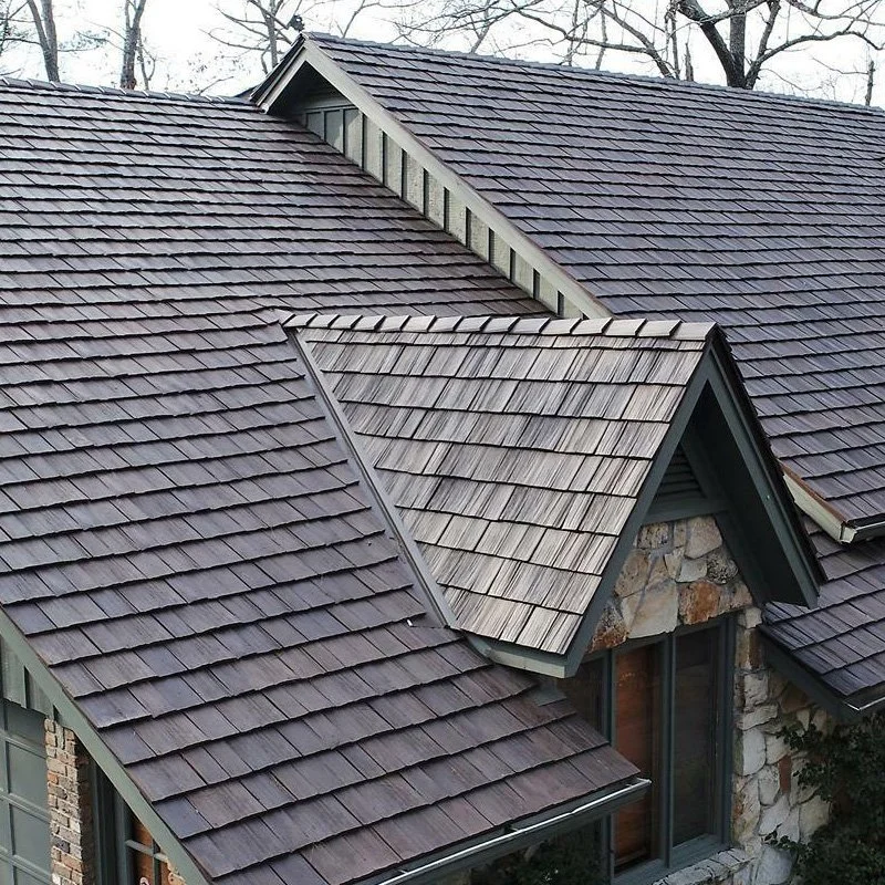 Close-up of a house roof with different sections of dark gray and gray shingles, including a dormer window with a stone and wood exterior.