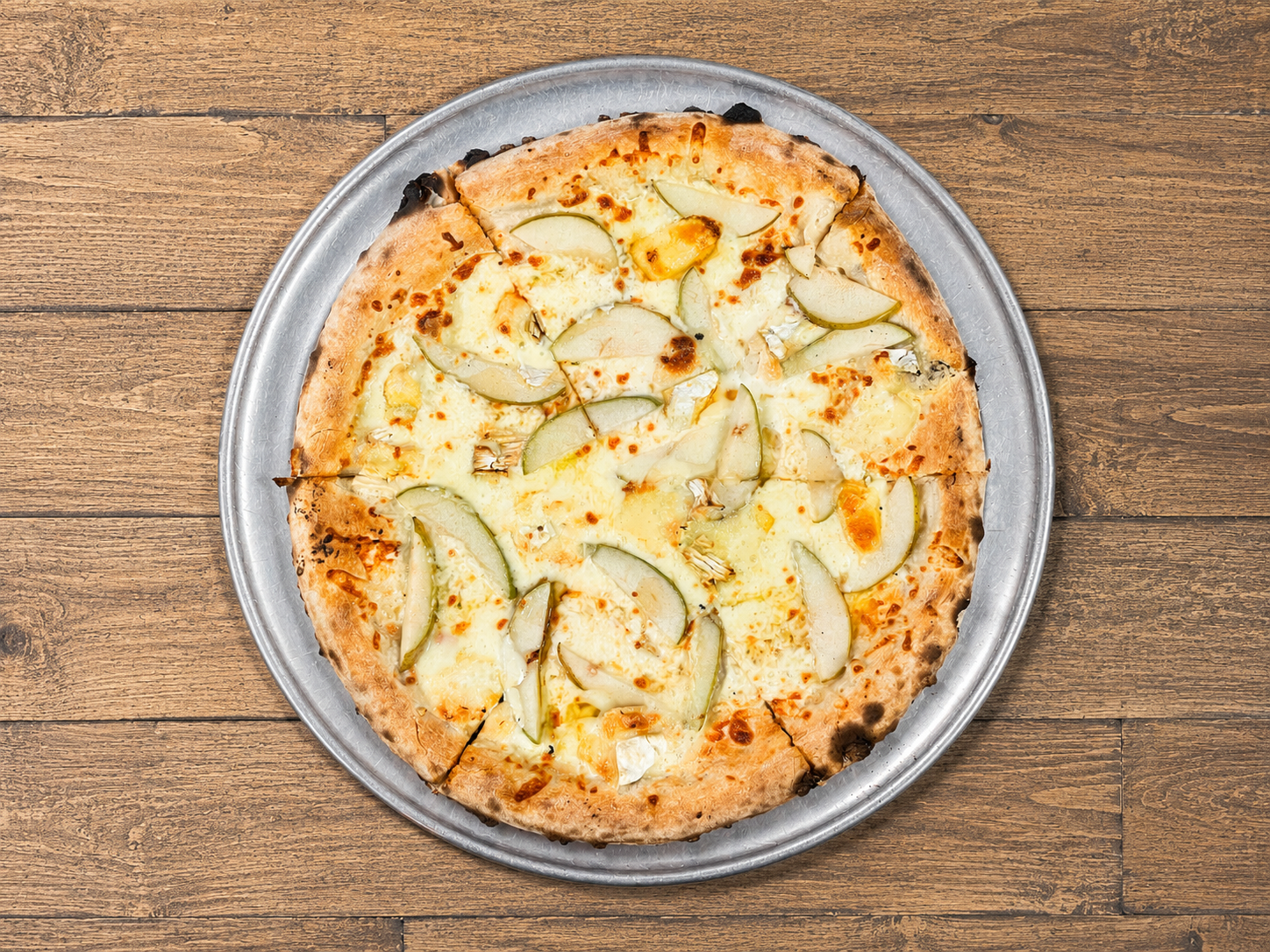 A cheese and pear pizza on a metal tray on a wooden surface