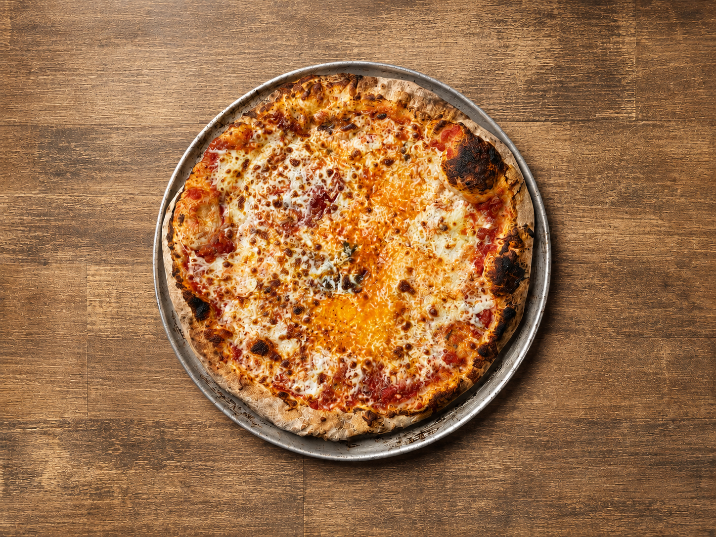 A pizza with melted cheese, tomato sauce, and toppings on a round silver tray placed on a wooden surface.